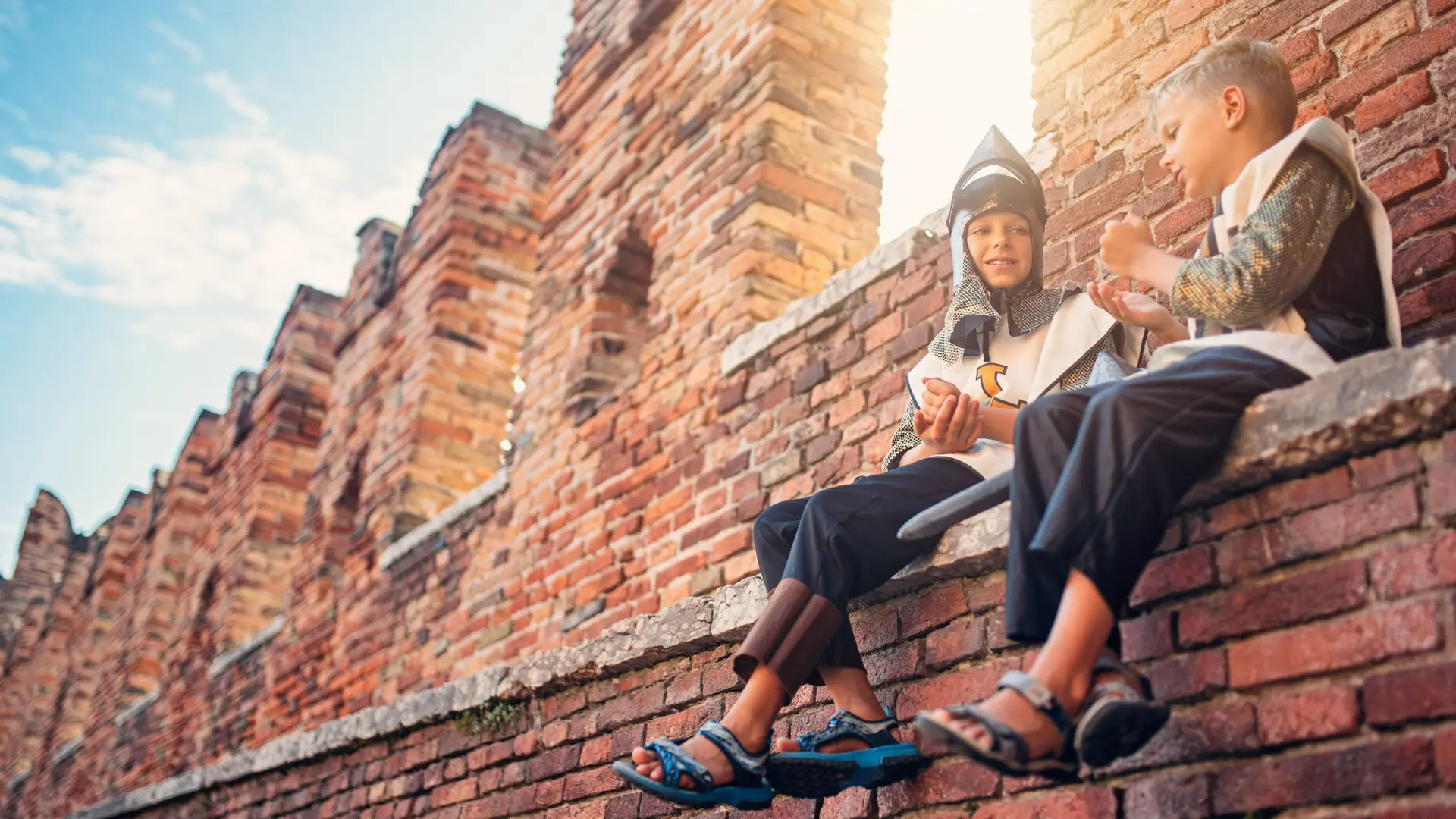 Zwei als Ritter verkleidete Jungen sitzen auf einer alten gemauerten Festungswand.