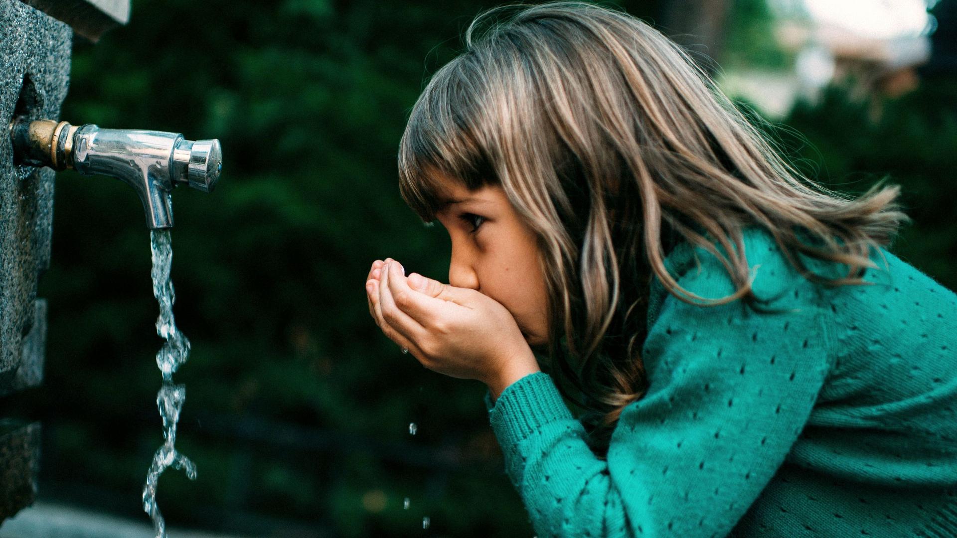 Ein Mädchen trinkt Wasser aus einem Trinkbrunnen in der Natur