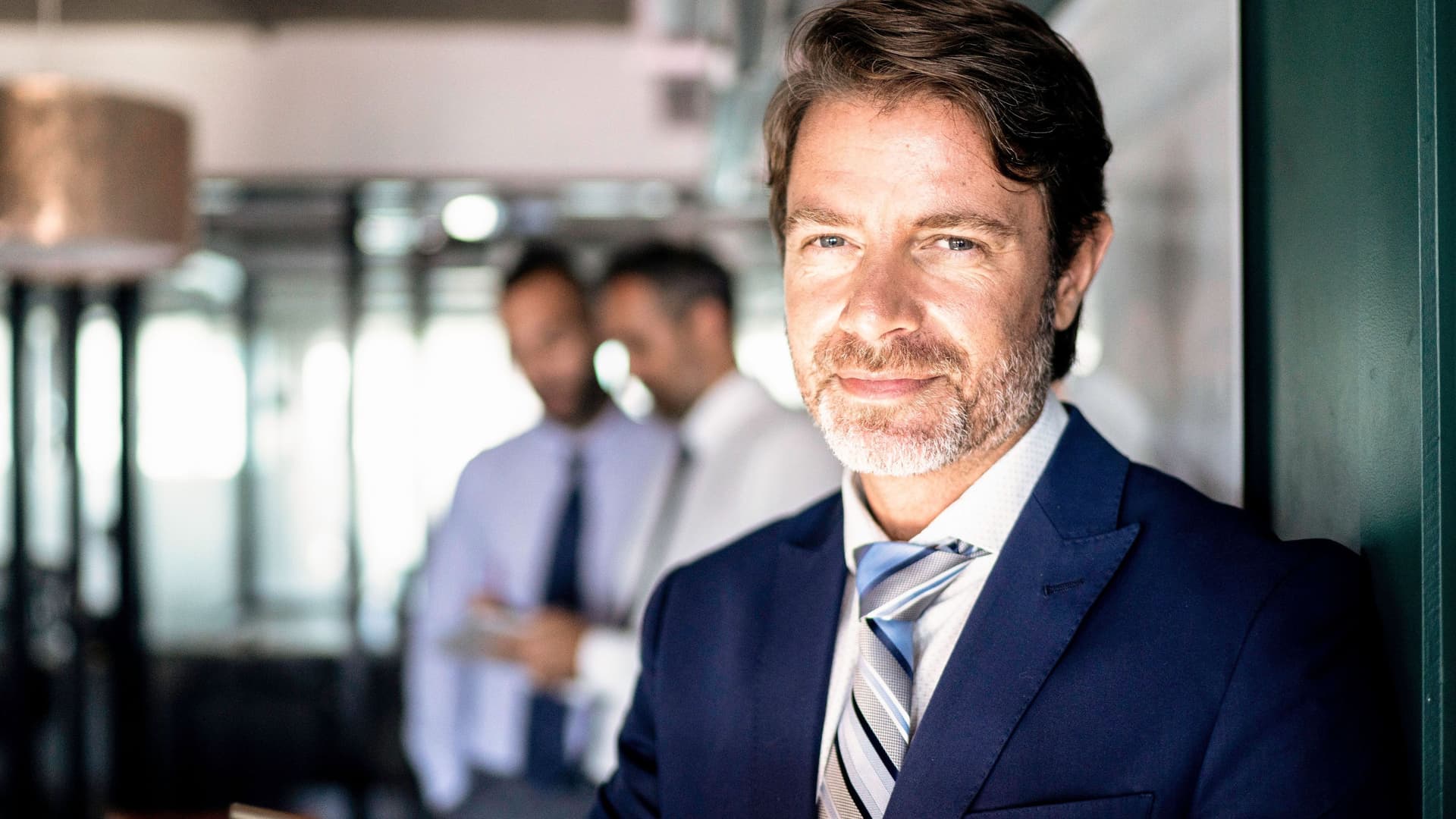Mann in Anzug mit Krawatte mit Blick in die Kamera, hält ein Tablett in der Hand.