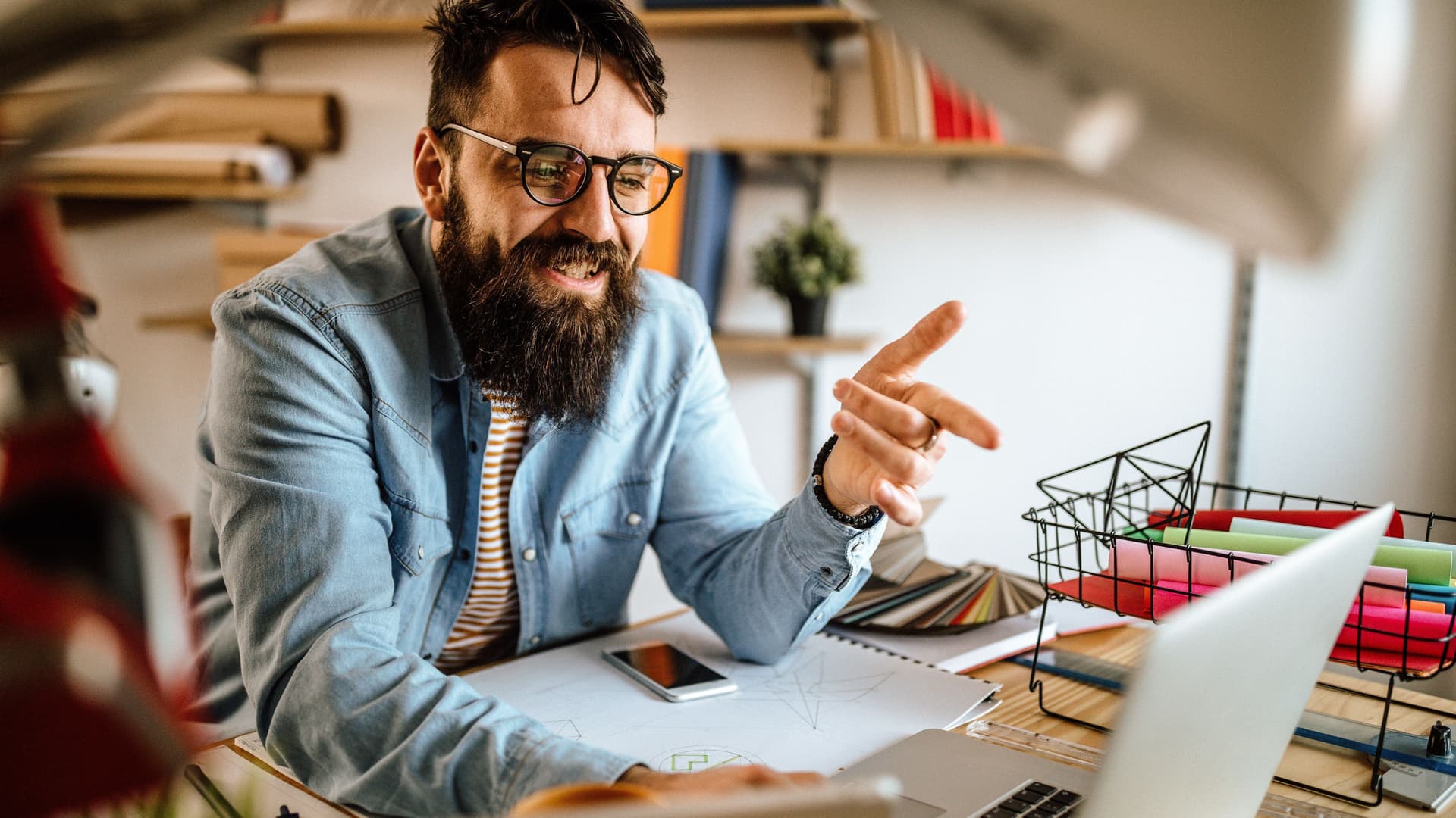 Foto eines lächelnden Mannes, der mit dem Finger auf einen aufgeklappten Laptop in einem Büro zeigt.