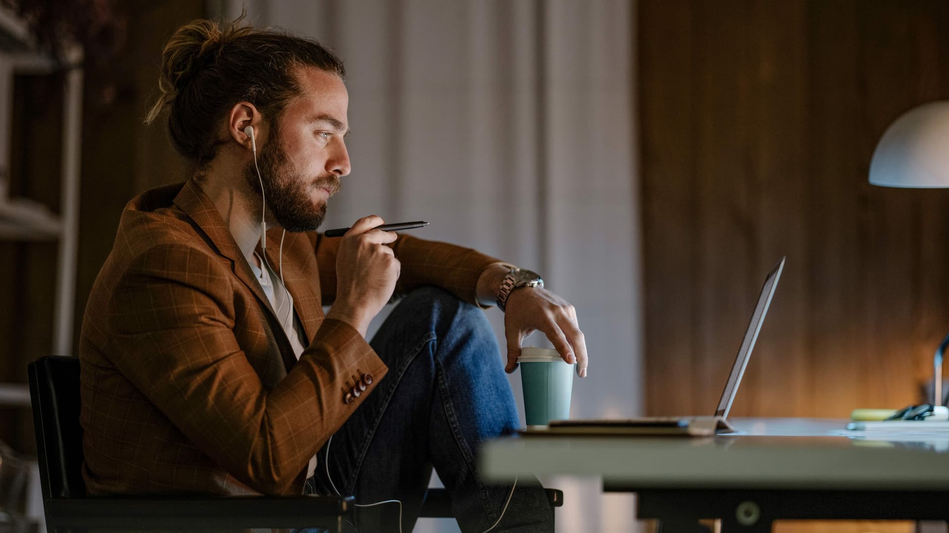 Seitenansicht eines jungen Mannes, der in den Abendstunden entspannt vor seinem Laptop sitzt und diesen anschaut.