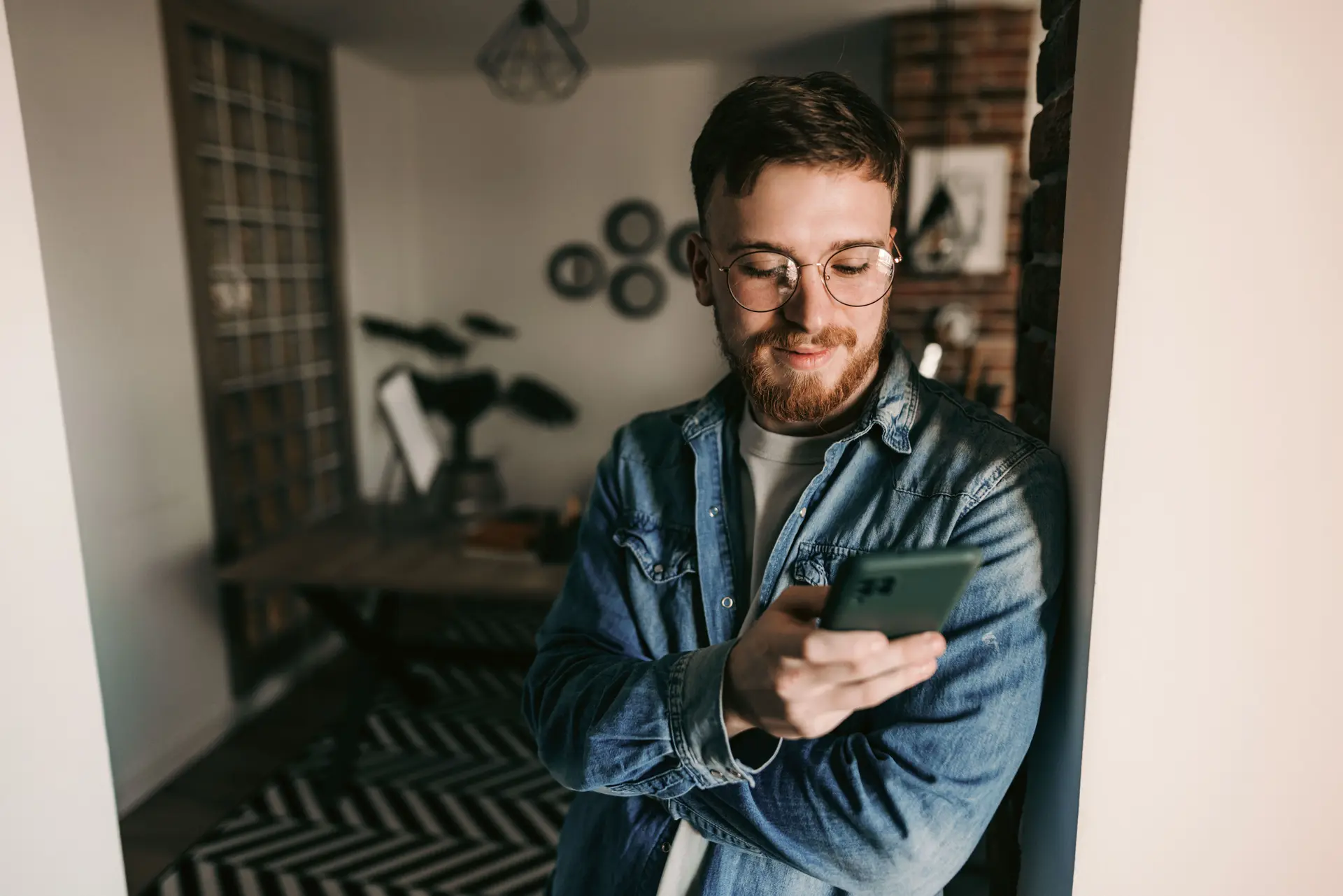 Junger Mann lehnt in einem Türrahmen und blickt in sein Smartphone