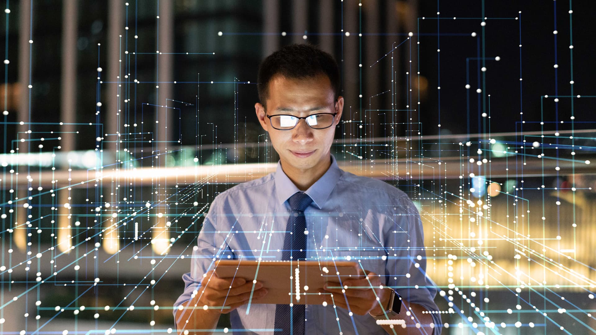Mann in Hemd und Krawatte mit Tablet in der Hand. Vor ihm sind verschieden vernetzte Lichtpunkte zu erkennen.