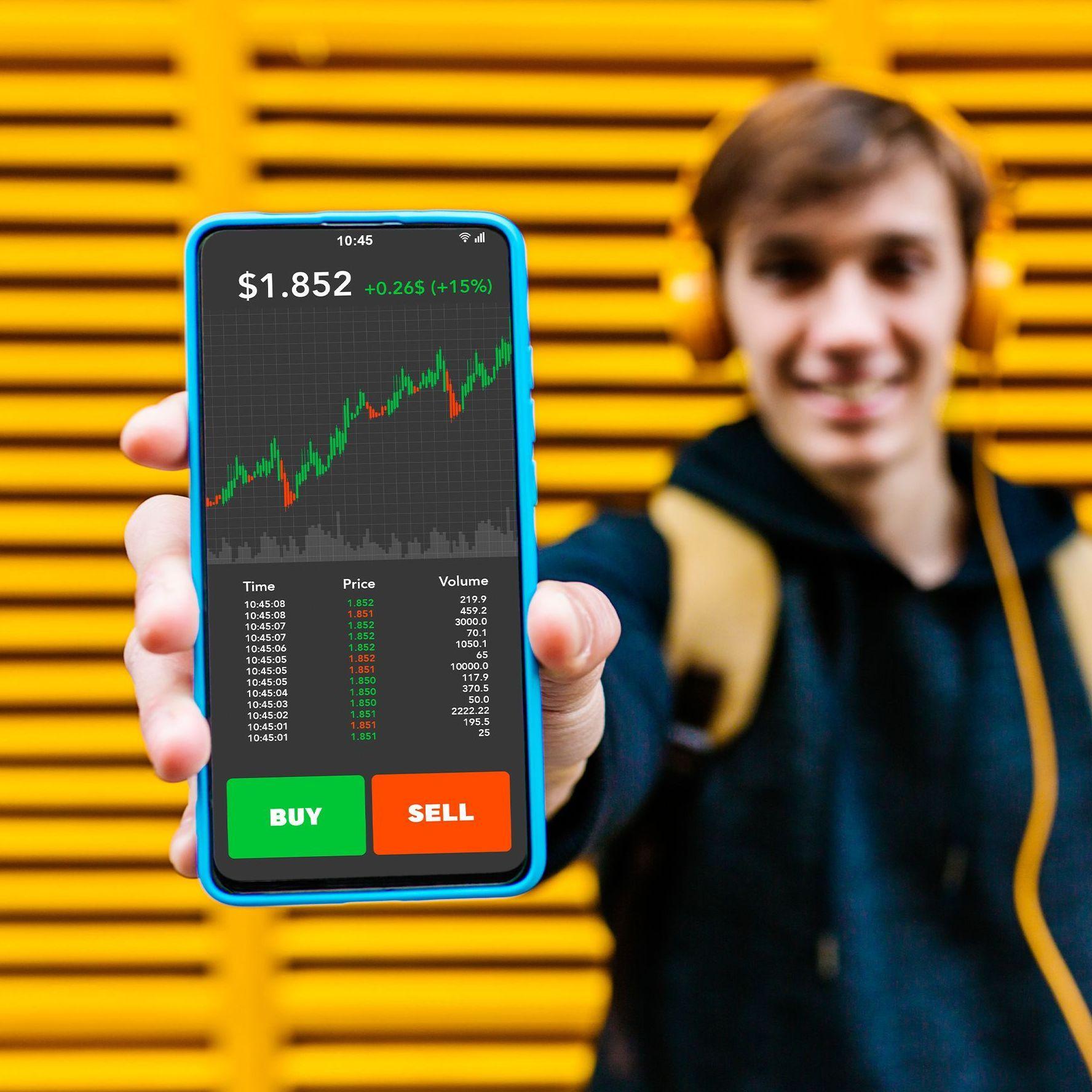 Ein junger Mann zeigt seinen Smartphone-Bildschirm mit einer Börseninvestitions-App in die Kamera. 