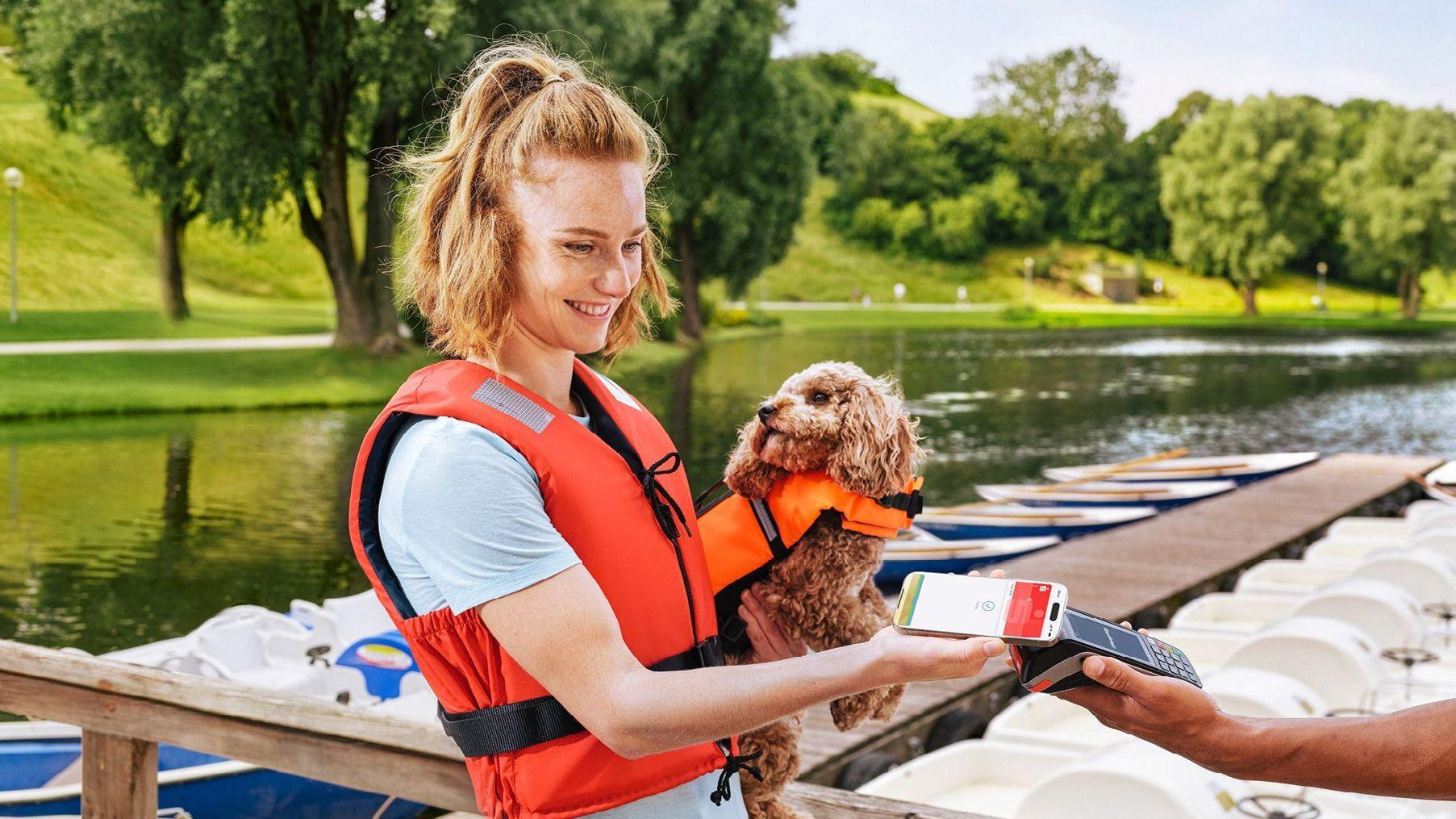 Frau bezahlt mit Smartphone mit Apple Pay und mit Hund im Arm.