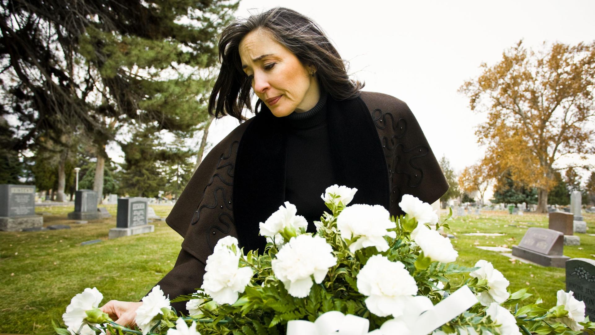 Eine Frau trauert an einem frischen Grab, das mit weißen Blumen geschmückt ist