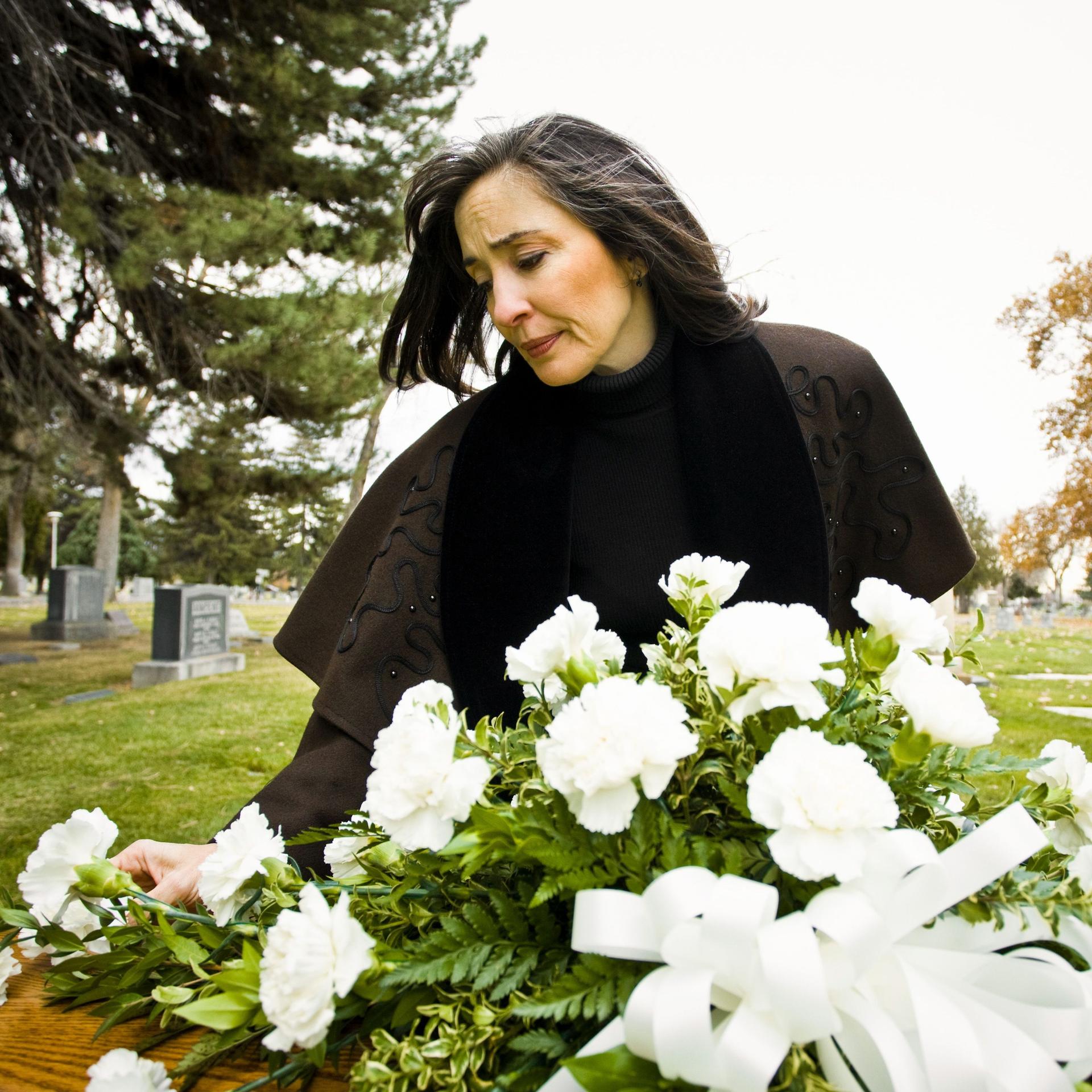 Eine Frau trauert an einem frischen Grab, das mit weißen Blumen geschmückt ist