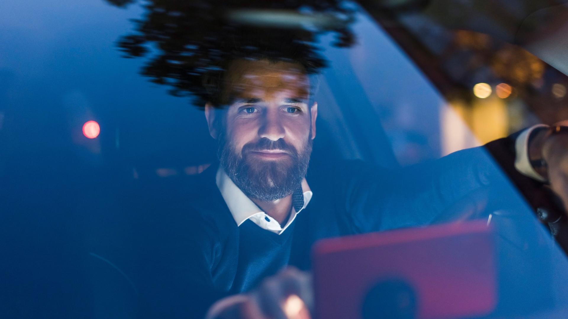 Ein Mann sitzt in seinem Auto und tippt auf sein Smartphone