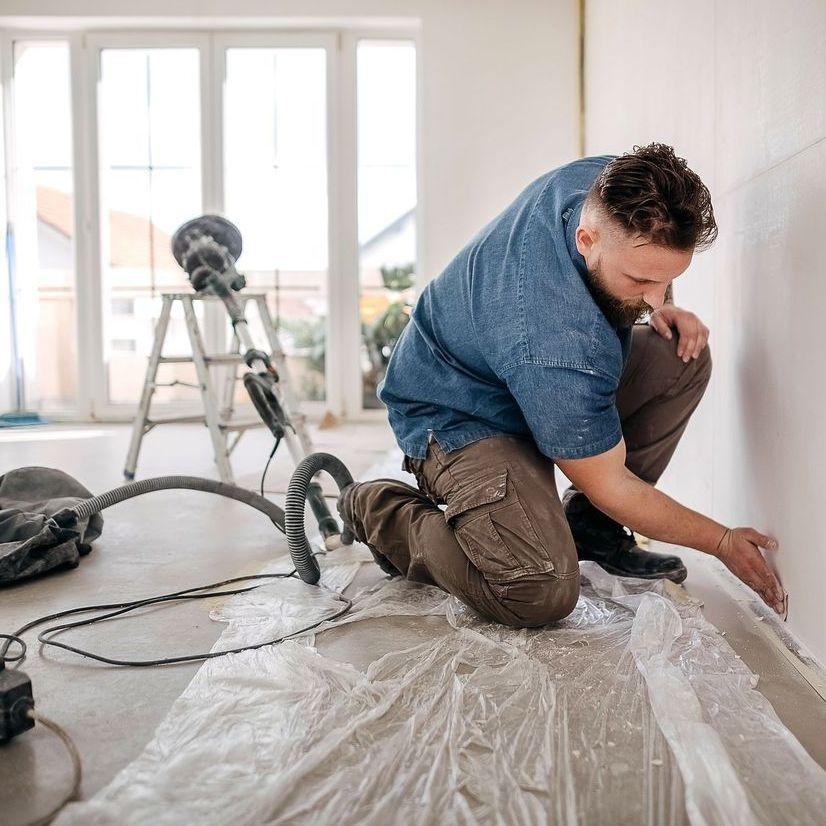 Ein Handwerker schleift auf einer Baustelle eines Privathauses eine Trockenbauwand. 


