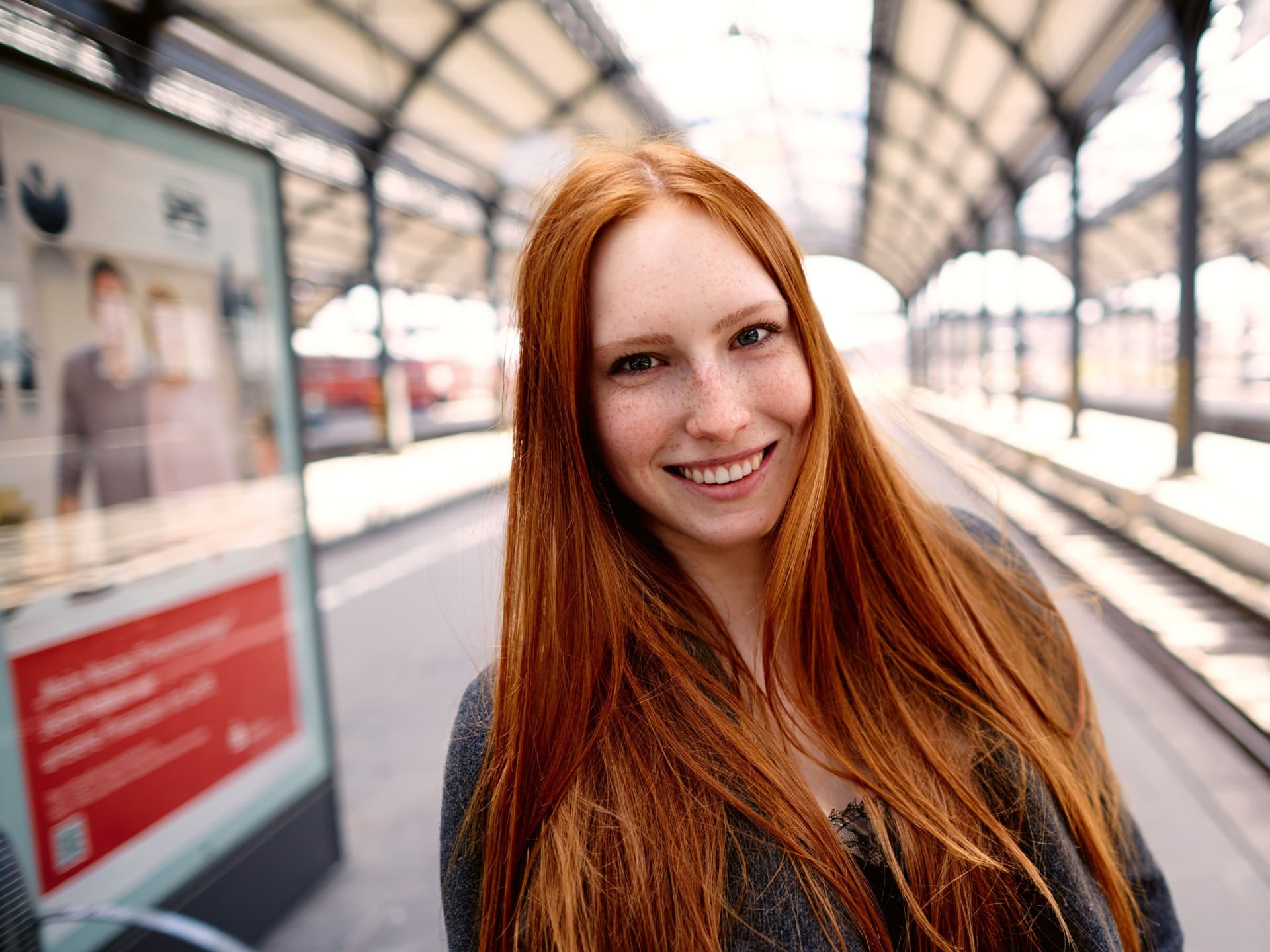 Eine Frau mit langen roten Haaren steht auf einem Bahnsteig.