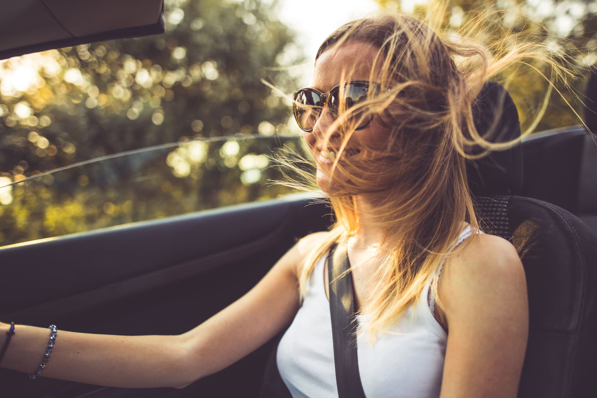 Eine junge, blonde Frau fährt mit wehendem Haar und Sonnenbrille Cabrio.