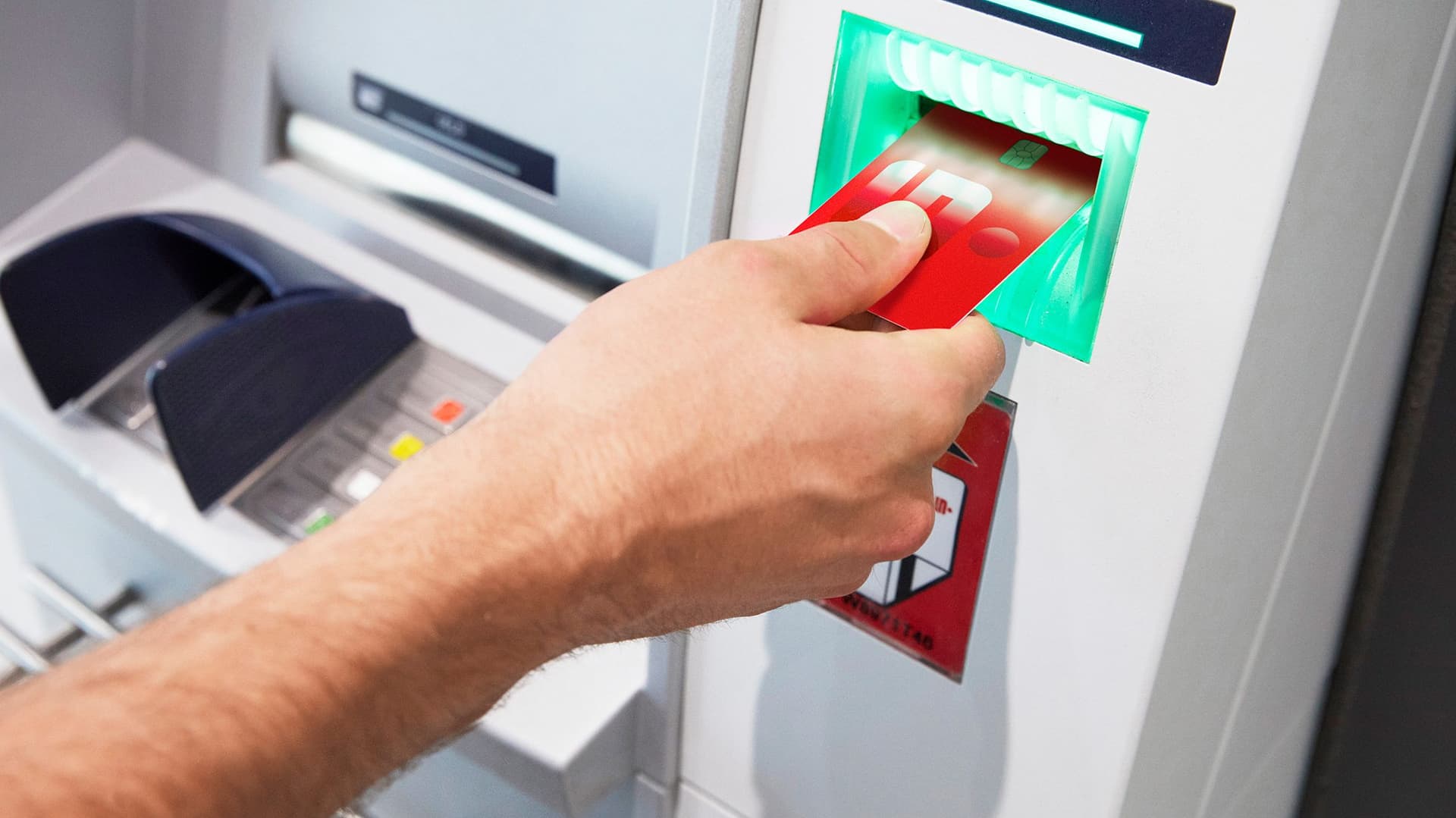 Hand steckt eine rote Sparkasse Debitkarte in den Kartenschlitz eines Geldautomaten.
