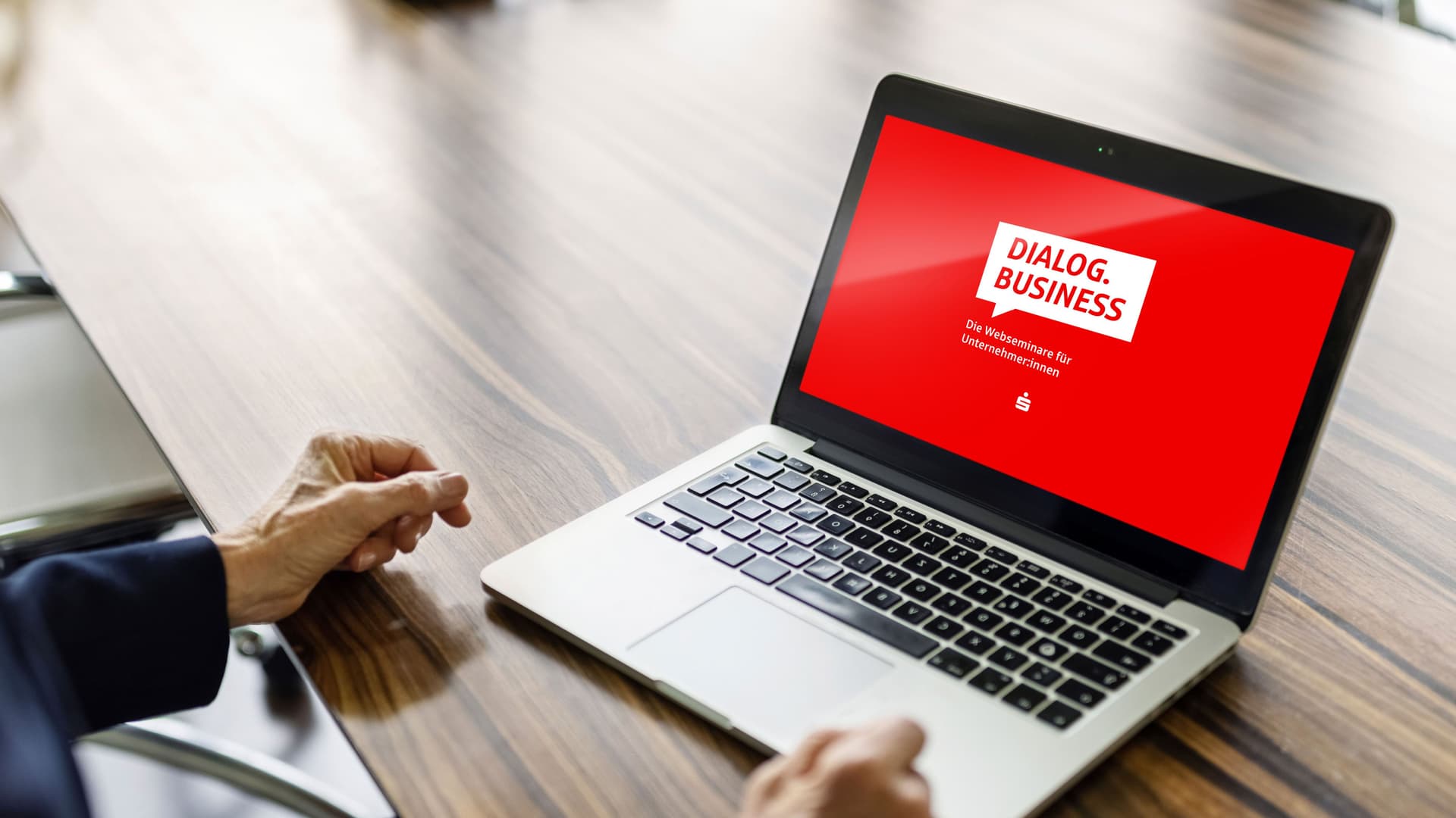 Eine Frau sitzt vor einem Laptop. Auf dem Bildschirm ist der Startscreen DialogBusiness.