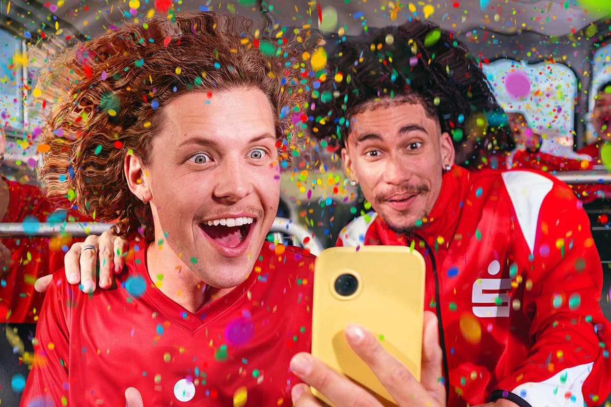 WERO Gewinnspiel Zwei jubelnde Personen in roten Trikots schauen begeistert auf ein Smartphone, während buntes Konfetti um sie herumfliegt.