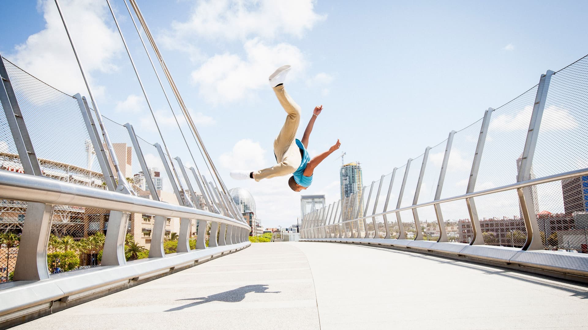Hebelprodukte: Spekulative Finanzinstrumente Junger Mann, der auf einer Fußgängerbrücke einen Salto schlägt. Er schwebt vor einem blauen Himmel in der Luft.