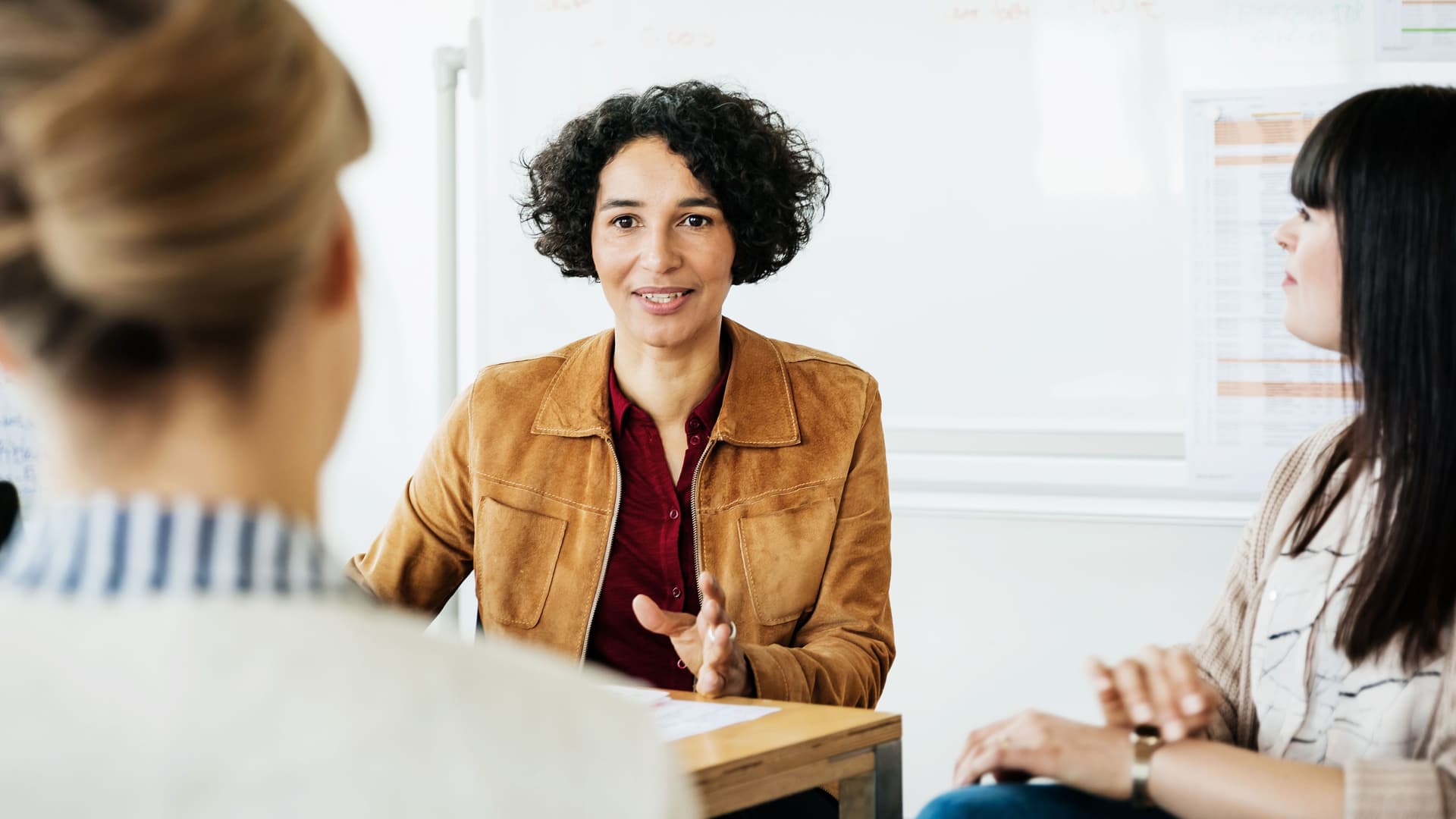 Sitution einer Gehaltsverhandlung: Drei Frauen sitzen an einem Tisch in einem hellen Raum und reden miteinander.