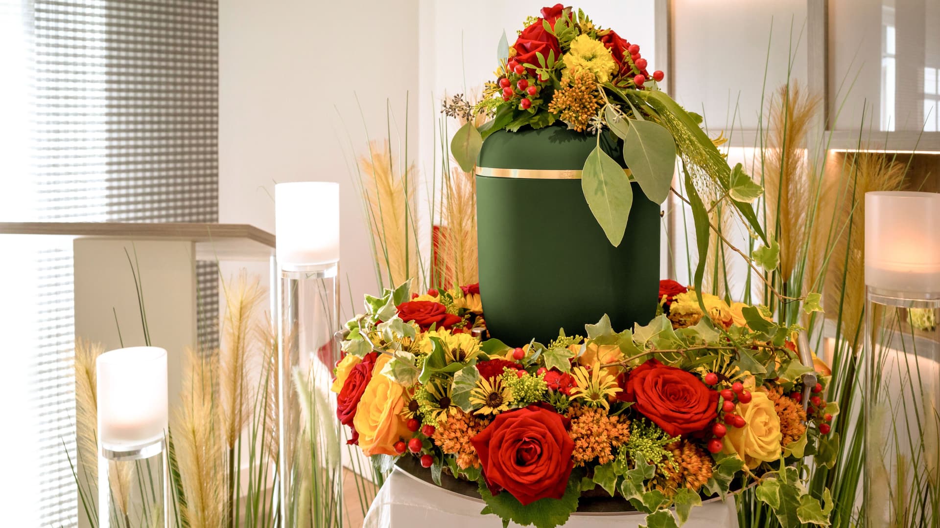 Eine blumengeschmueckte Urne steht aufgebahrt auf einem Sarg