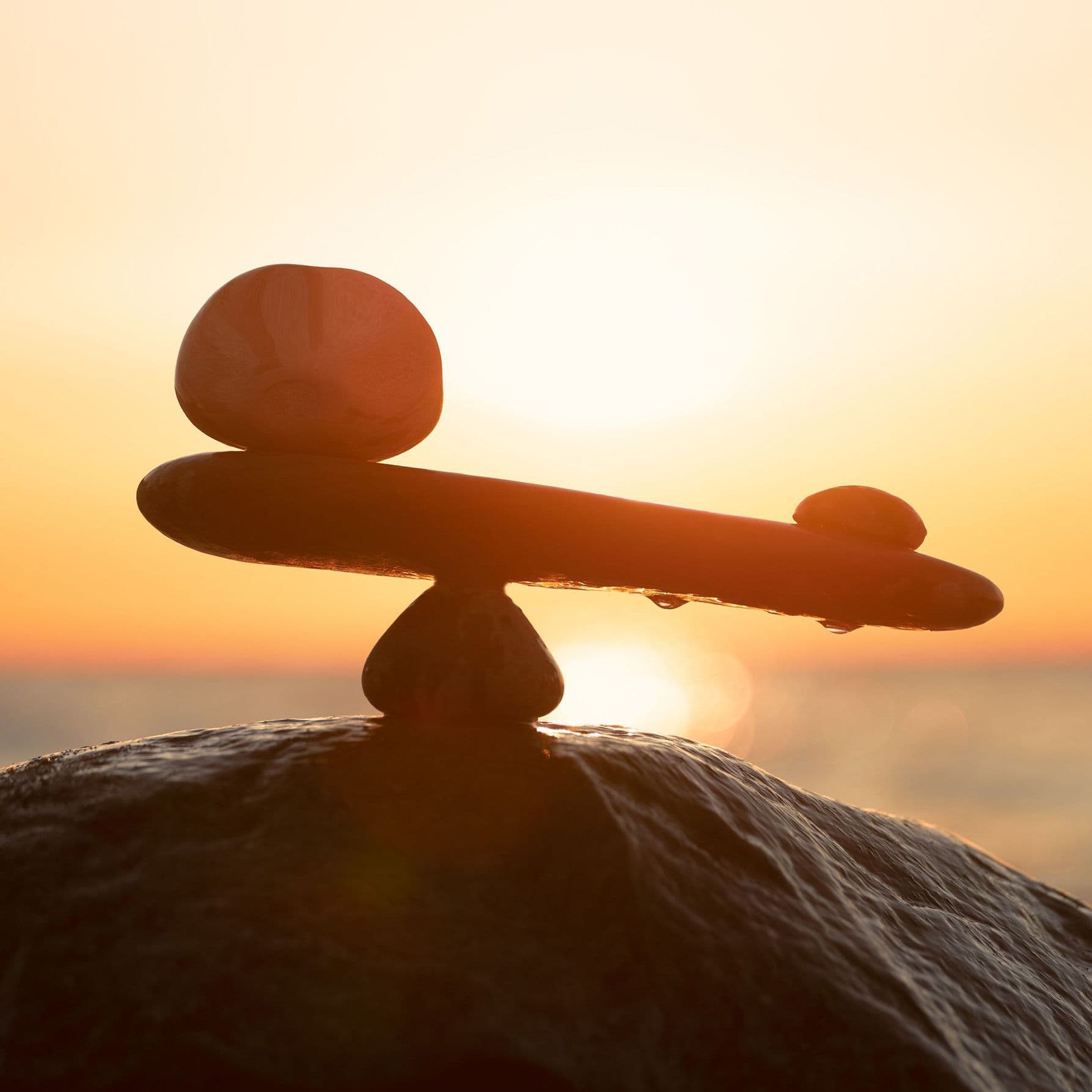 Auf dem Bild sind mehrere Steine zu sehen, die in einer Balance angeordnet sind. Im Hintergrund geht die Sonne unter, und das warme Licht erzeugt eine ruhige, natürliche Stimmung.
