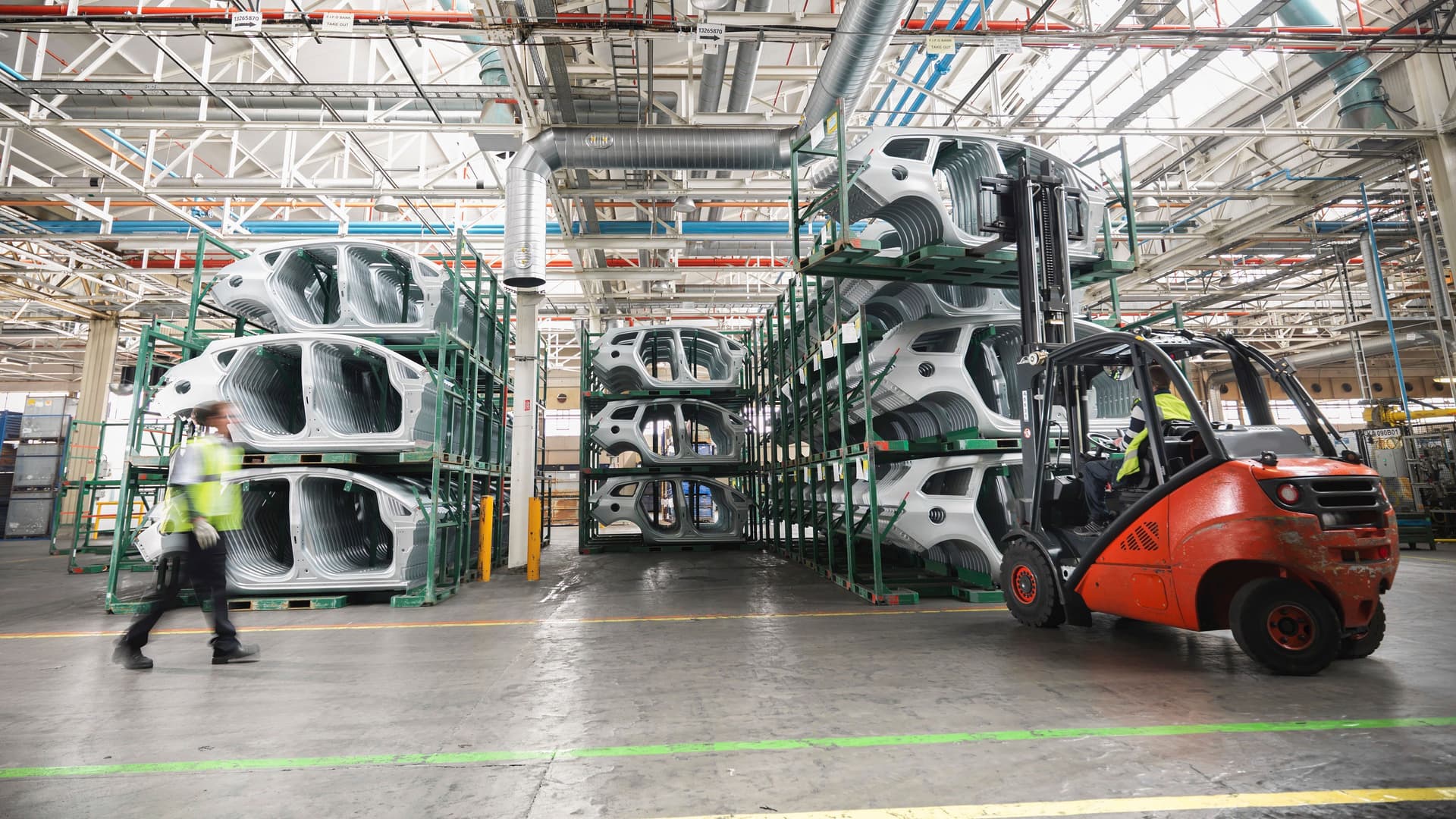 Auto Chassis in einer Lagerhalle einer modernen Fabrik. Davor steht ein Gabelstapler und ein Arbeiter mit Helm
