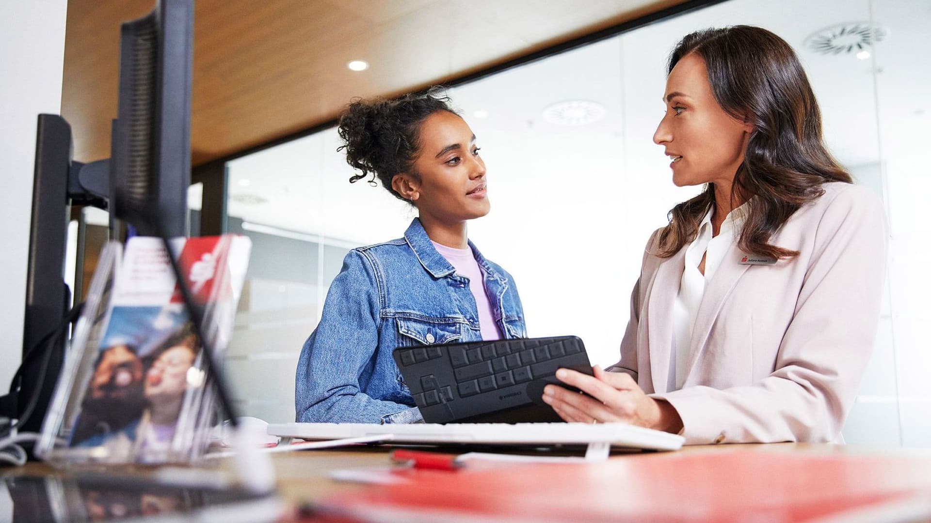 Eine Sparkassenberaterin mit einem Tablet in der Hand spricht konzentriert mit einer jungen Frau, die interessiert zuhört.