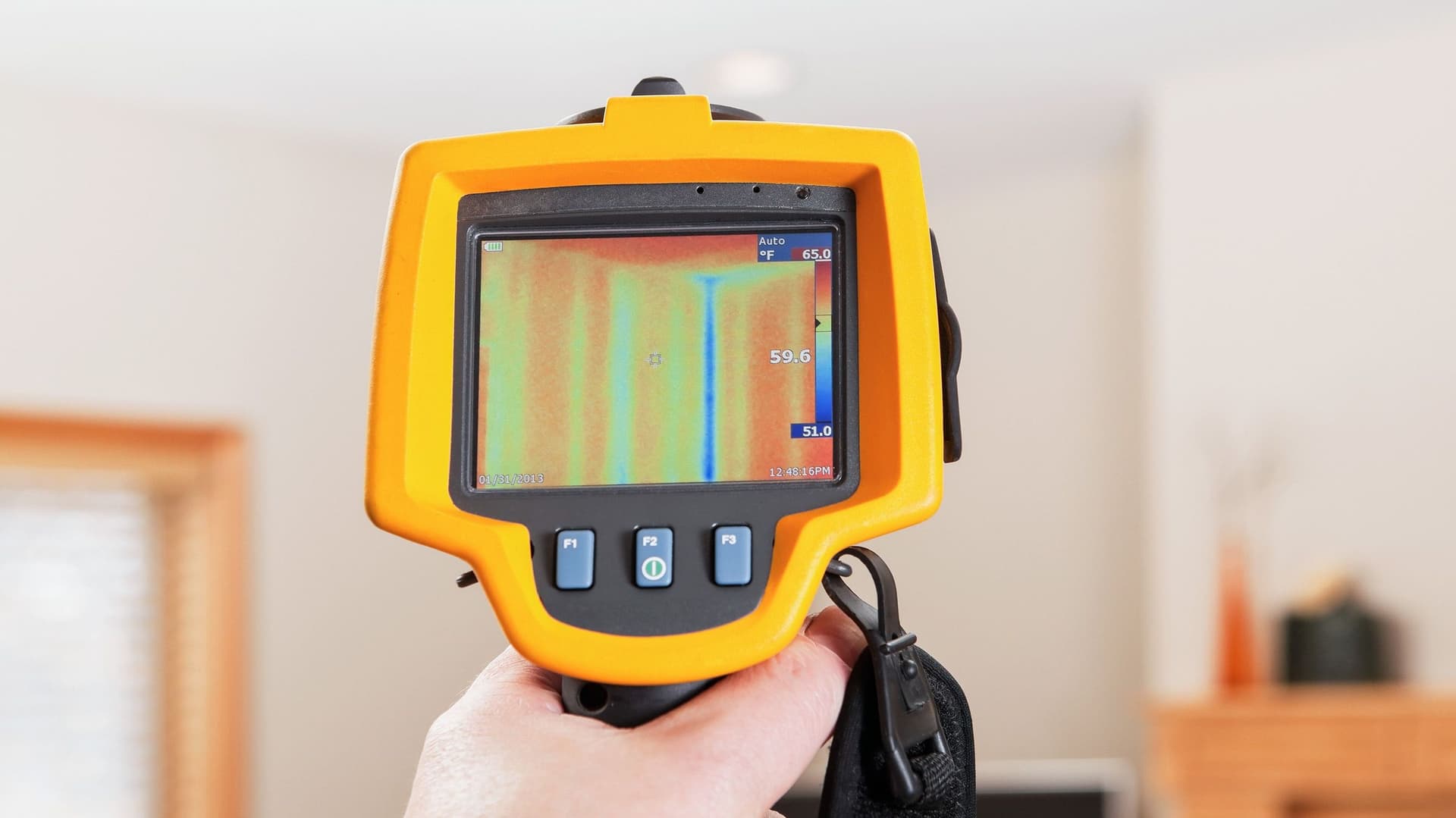 Das Bild zeigt eine Wärmebildkamera-Ansicht einer Wohnung, auf der eine Wand zu sehen ist. Die Temperaturverteilung wird durch ein Farbcode-System dargestellt, das warme Bereiche in Rot und kühlere Bereiche in Blau anzeigt.