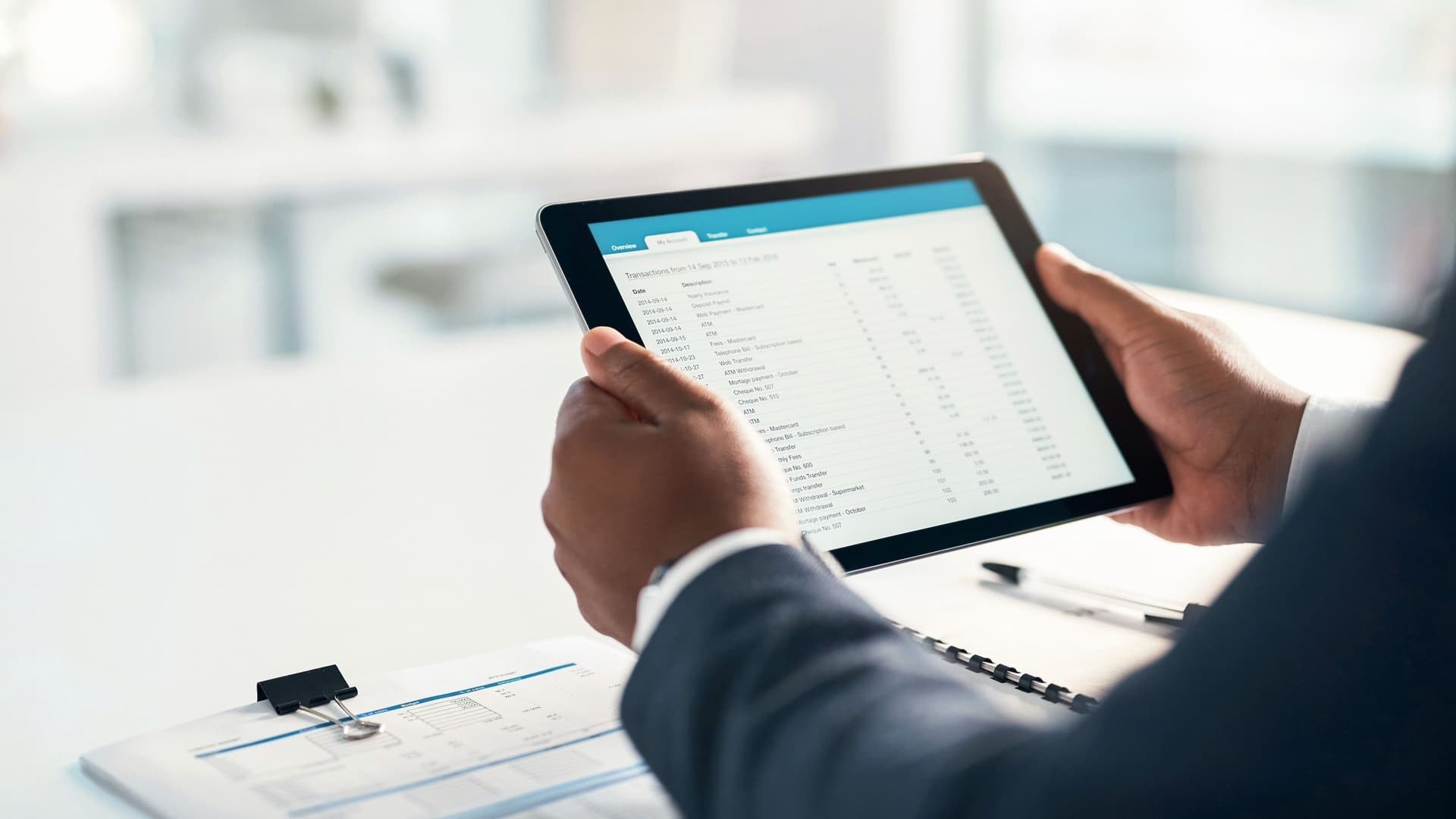 Blick über die Schulter einer Person in Anzug auf einen Tablet-Computer in deren Händen