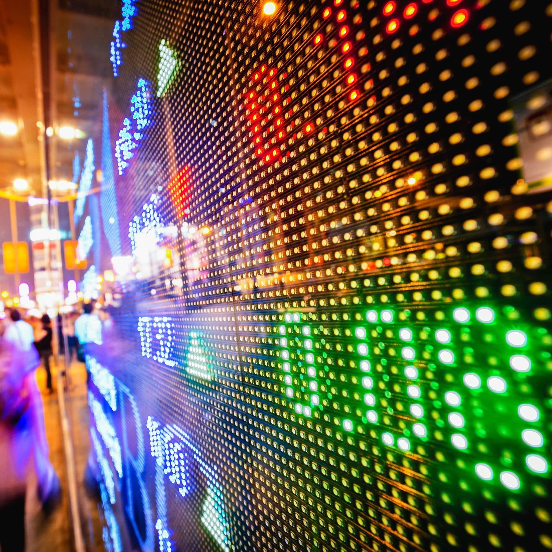 LED Anzeige von Börsenkursen auf einer großen Schaufensterfront. Unscharf laufen Menschen in einer Abendstimmung den Bürgersteig entlang.