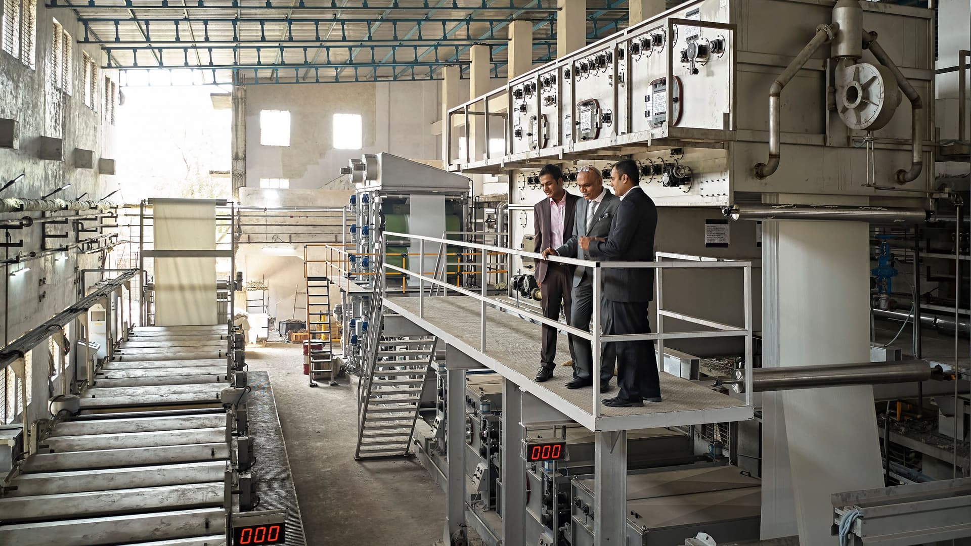 Drei Männer im Anzug, die auf einer erhöhten Plattform steht und das Fabriklayout in der Färberei und Druckerei in Mumbai studieren.