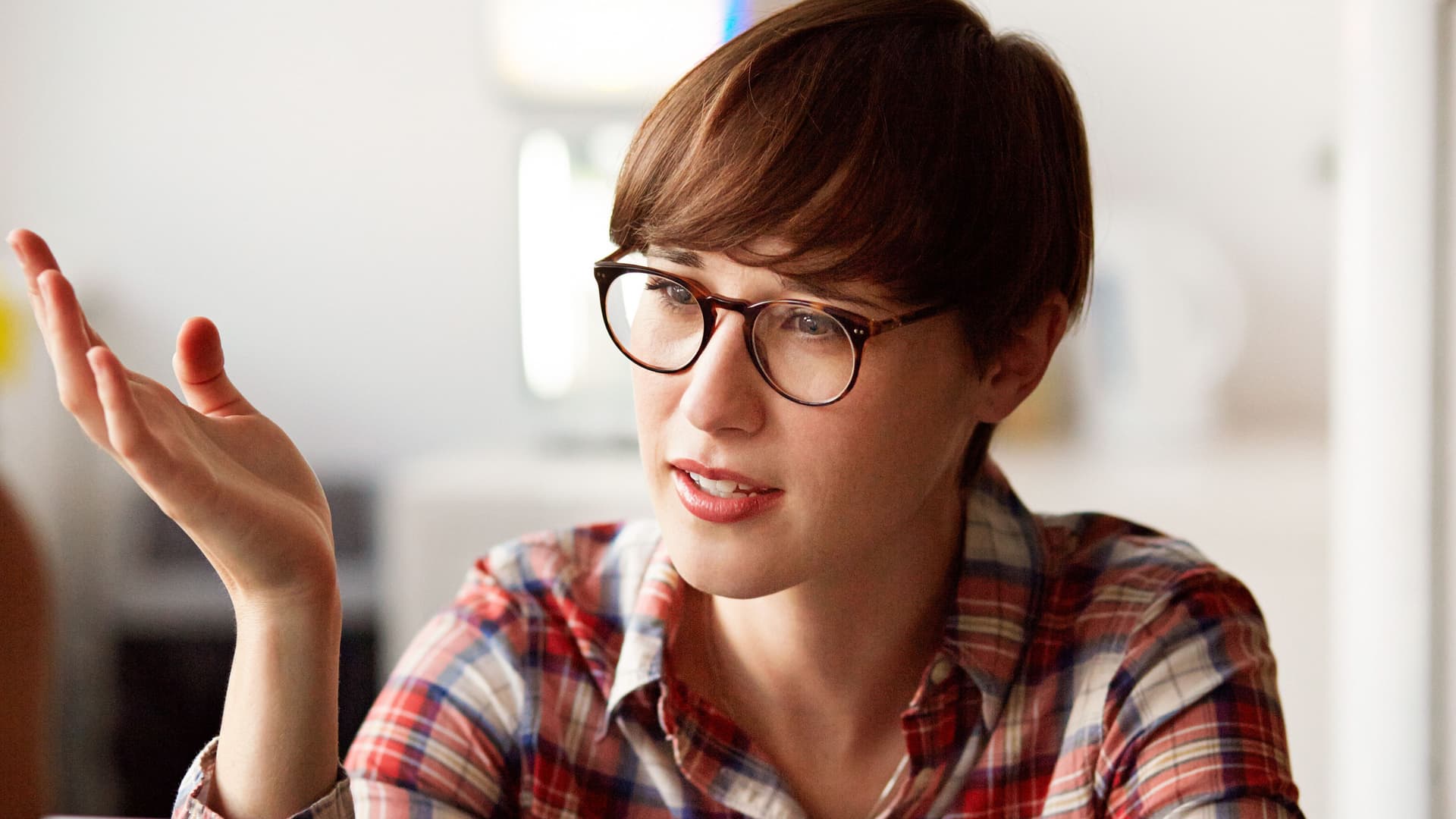 Junge Frau sitzt hinter einem Laptop, unterhält sich und gestikuliert dabei mit den Händen.