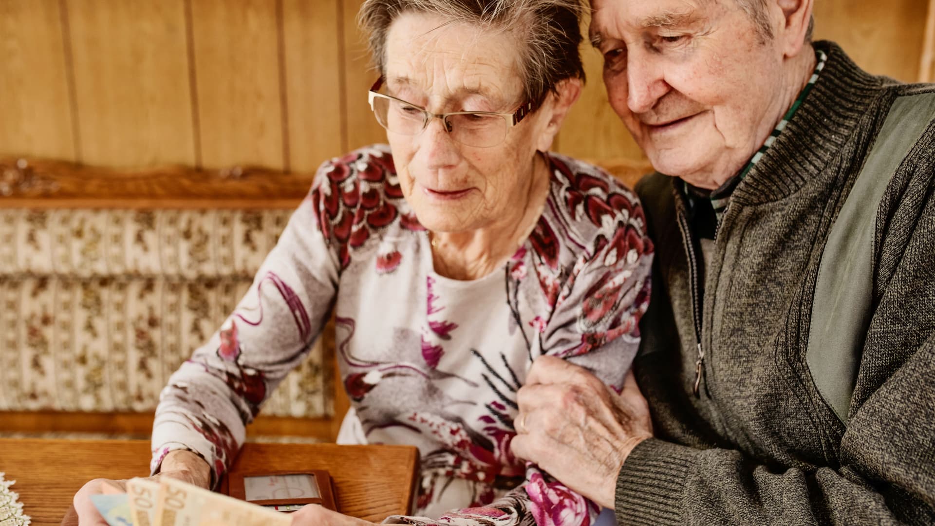 Älteres Paar umarmt sich und betrachtet Geld in der Hand der Frau.