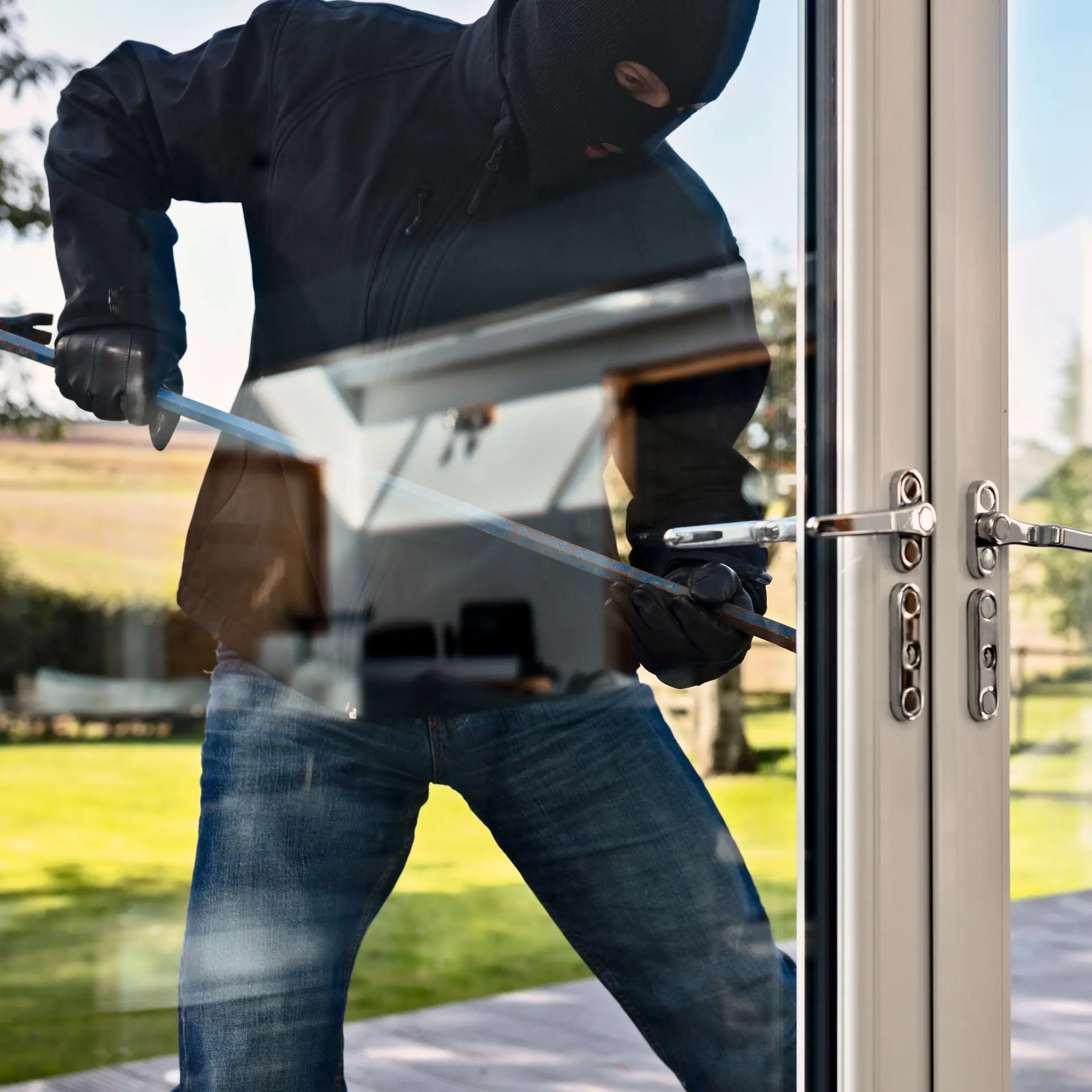 Vermummter Einbrecher steht vor Gartentür und versucht mit einem Brecheisen diese aufzuhebeln.