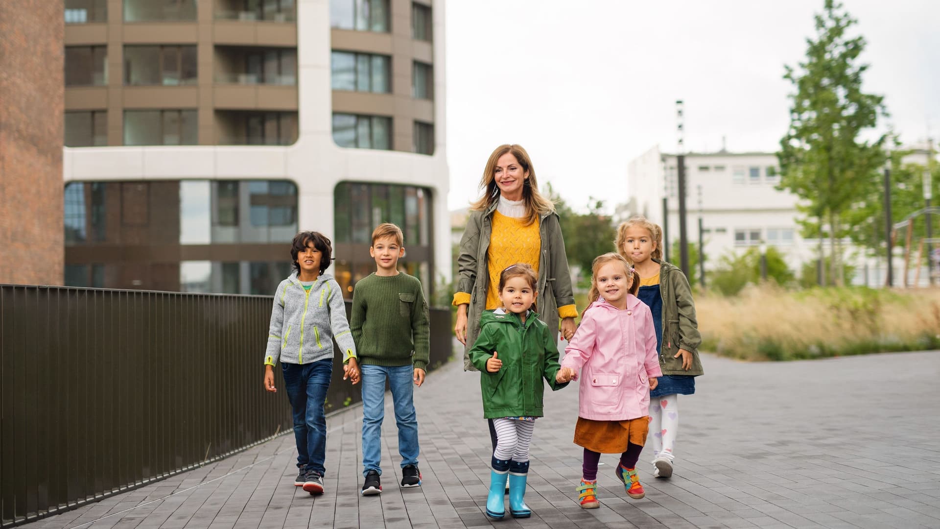Eine Erzieherin läuft mit einer Gruppe von 5 Kindern durch eine urbane Landschaft