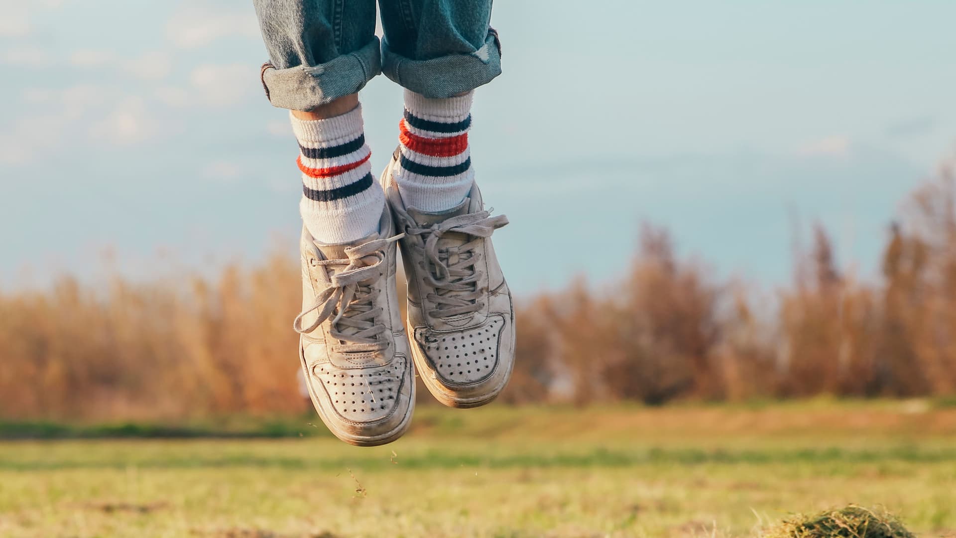 Zwei springenden Füße mit Ringelsocken und Turnschuhen. Im Hintergrund eine Wiese und Sträucher.