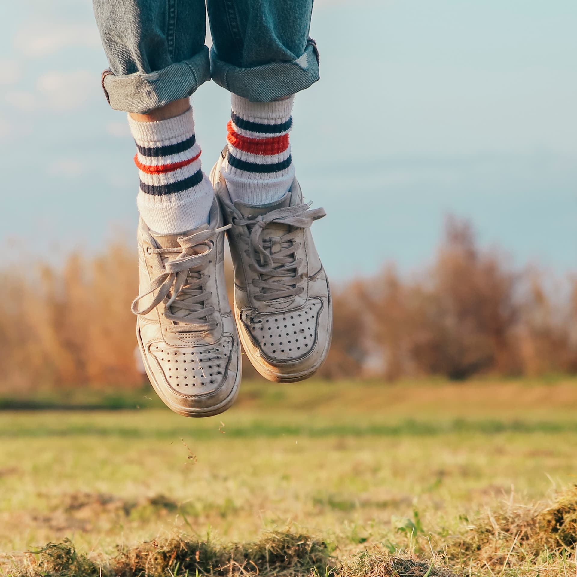 Zwei springenden Füße mit Ringelsocken und Turnschuhen. Im Hintergrund eine Wiese und Sträucher.
