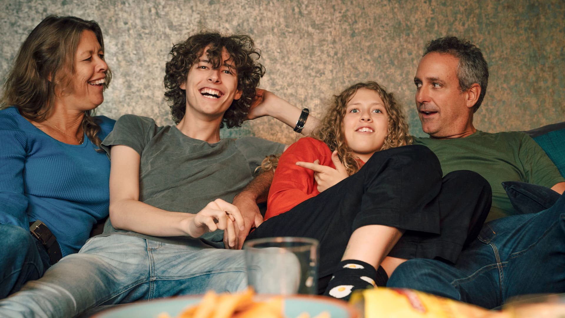 Fröhliche Familie auf dem Sofa beim Fernsehen mit Chips