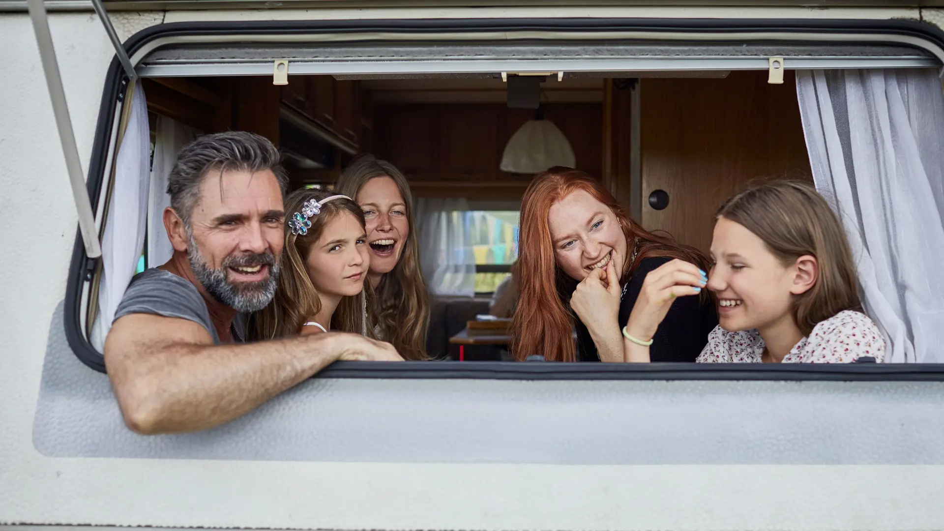 Eine Familie schaut aus dem Heckfenster eines Wohnmobils. Sie lachen.