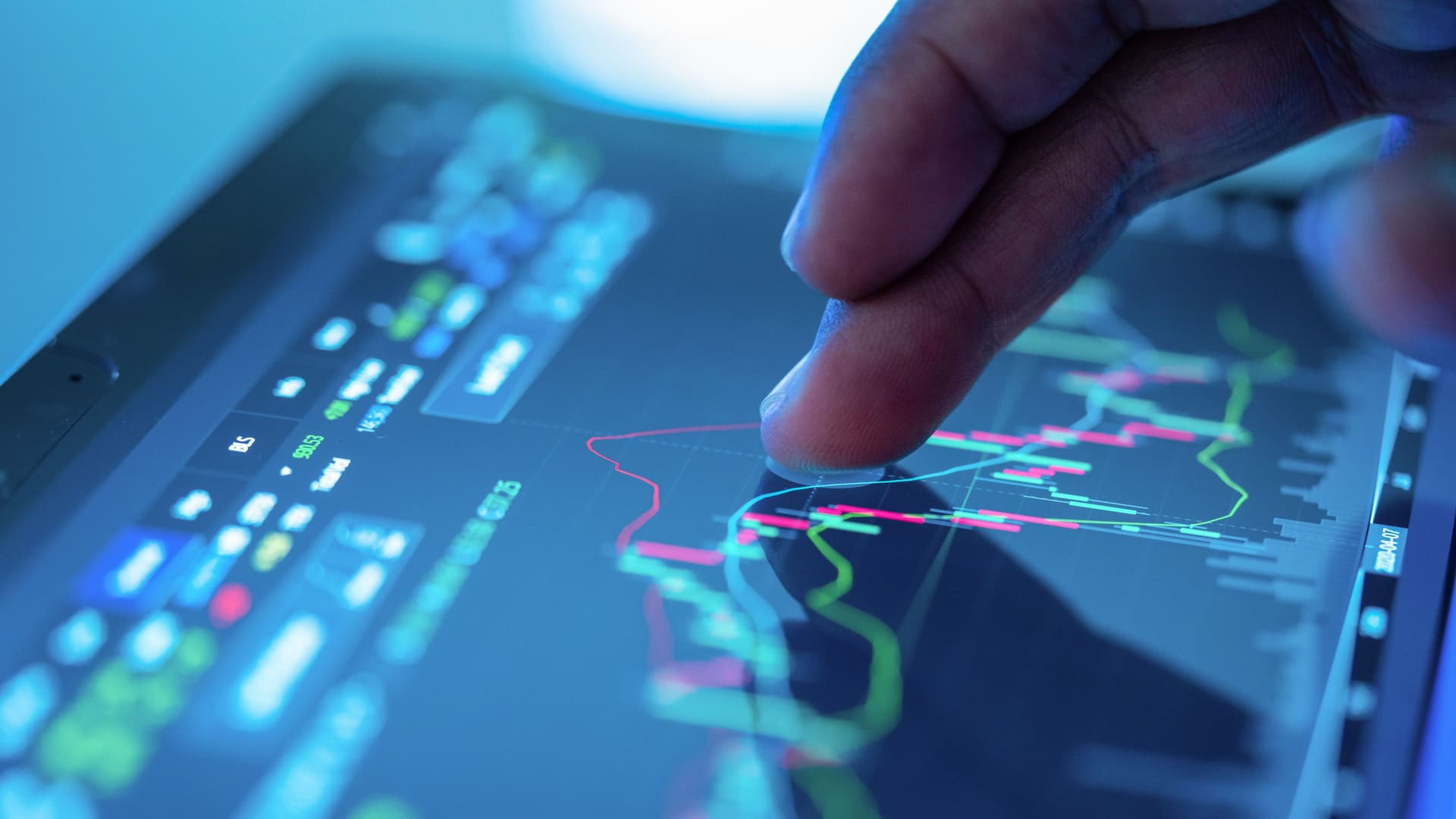 Nahaufnahme einer Hand, die das Display eines Tablet-Computers berührt. Auf dem Bildschirm sind mehrere farbige Graphen und Zahlen zu sehen.