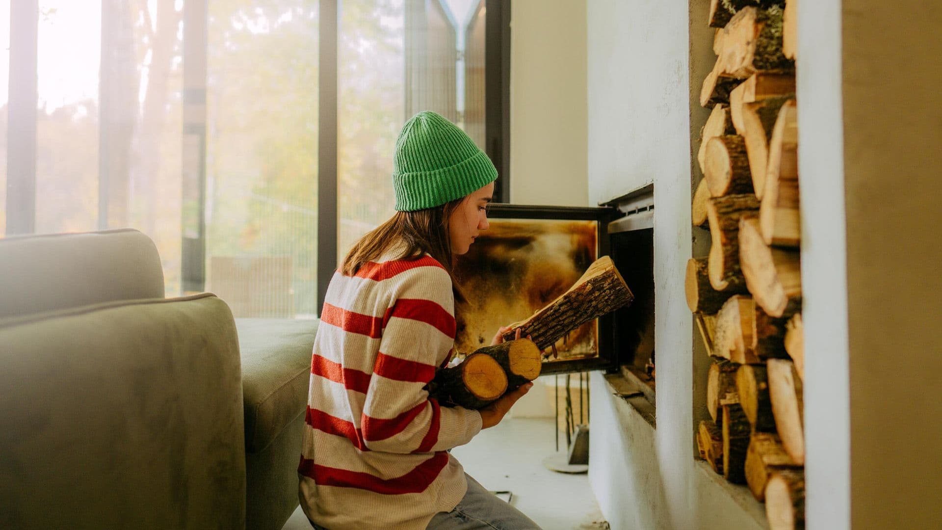 Frau legt Holzscheite in einen brennenden Kaminofen, um ihn zu befeuern