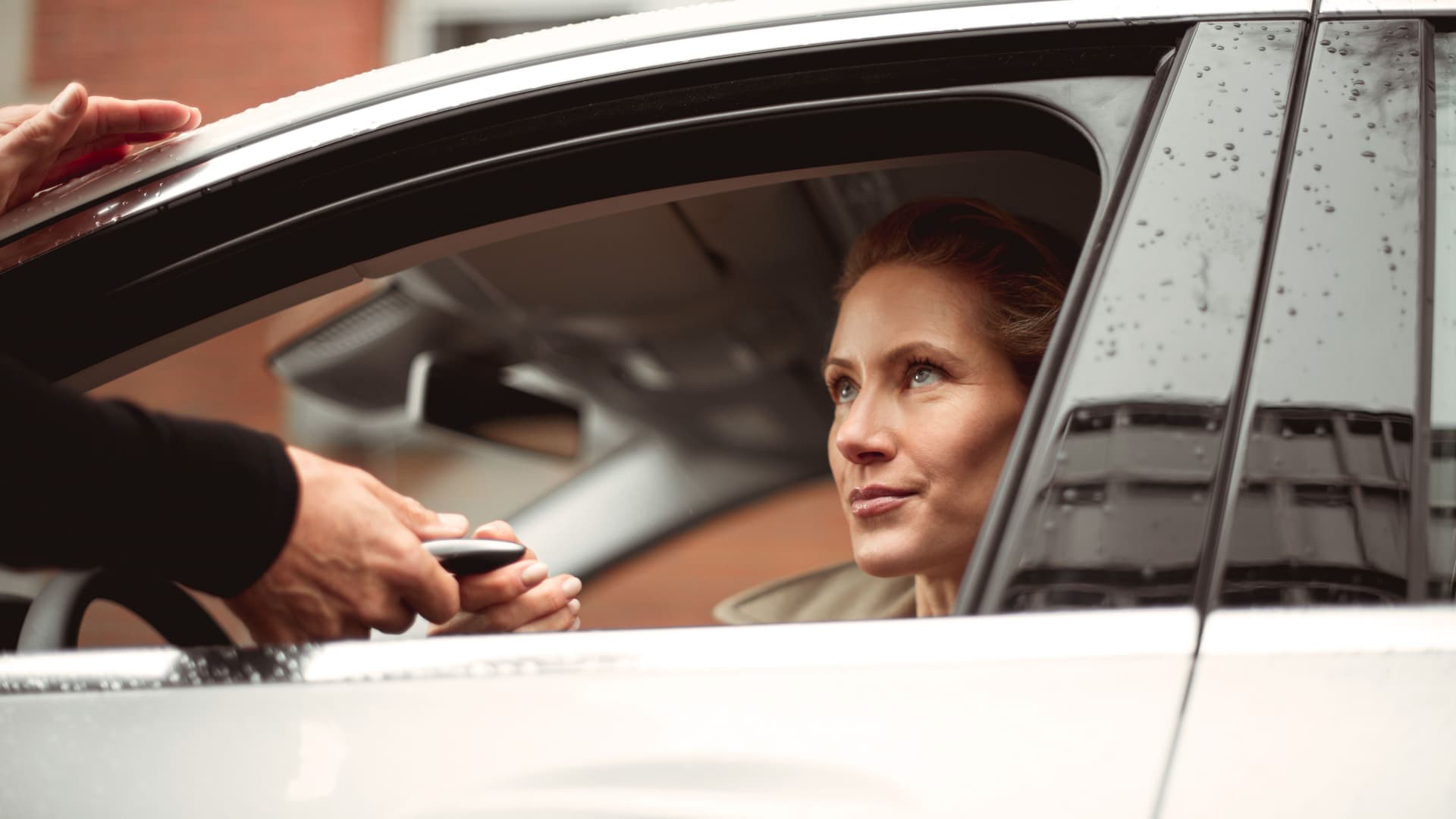 Eine Frau sitzt am Steuer einen Autos und erhält durch das offene Fahrerfenster den Autoschlüssel.