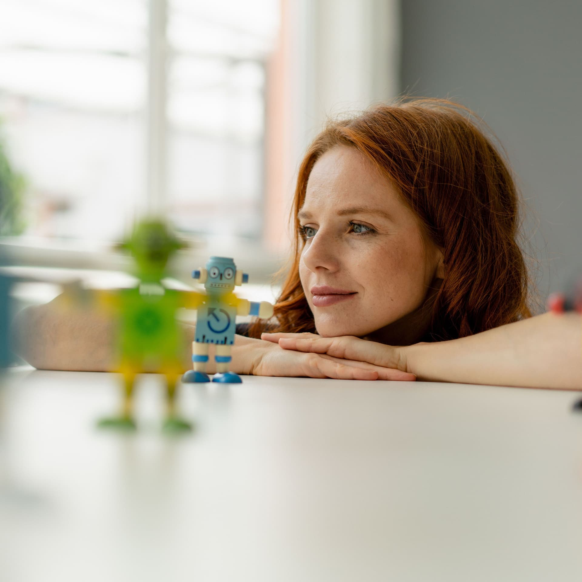 Porträt einer jungen Frau, die sich Miniaturroboter aus Holz auf einer Tischplatte.ansieht.