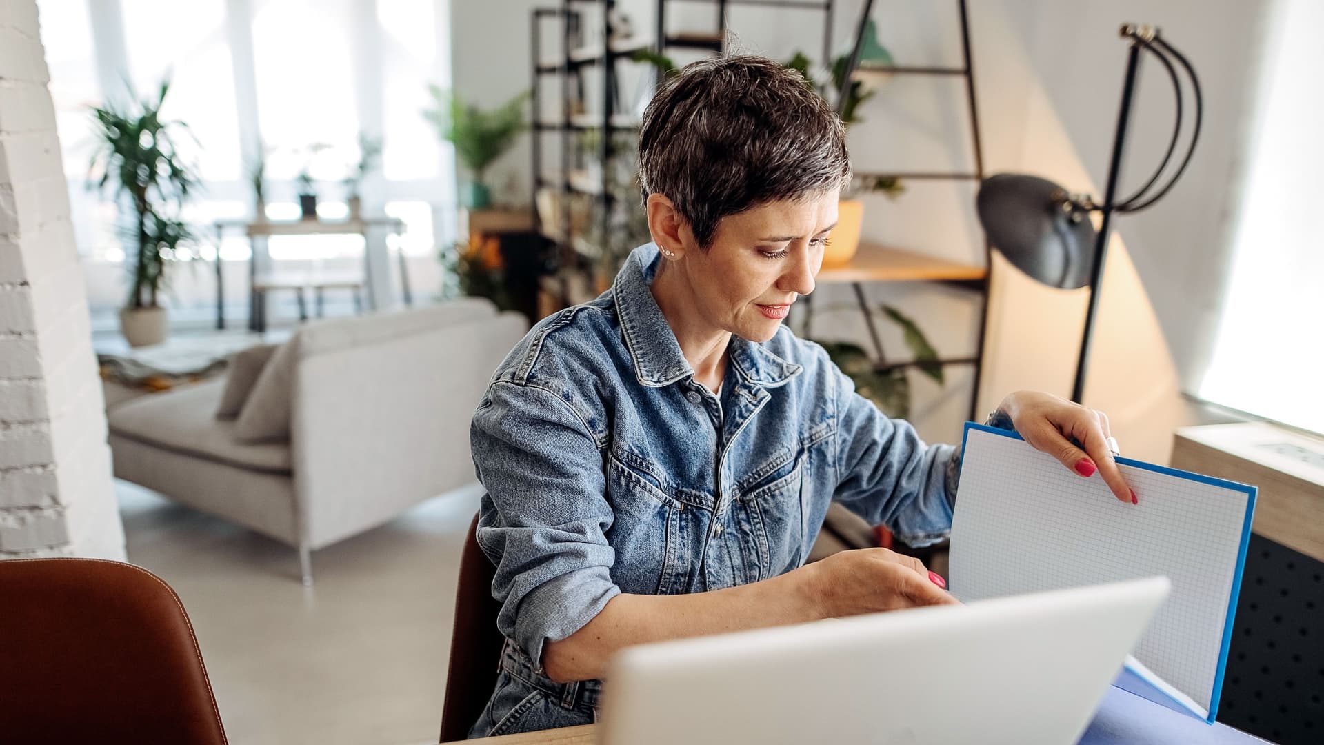 Aufnahme einer jungen Frau, die einen Laptop benutzt und Papierkram durchgeht, während sie von zu Hause aus arbeitet