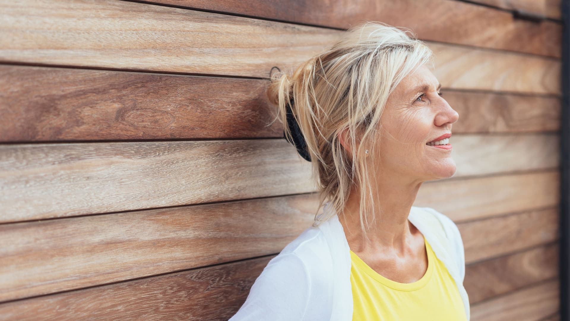 Eine reifere Frau in einer seitlichen Porträtaufnahme. Ihr Kopf ist gegen eine Holzwand gelehnt.