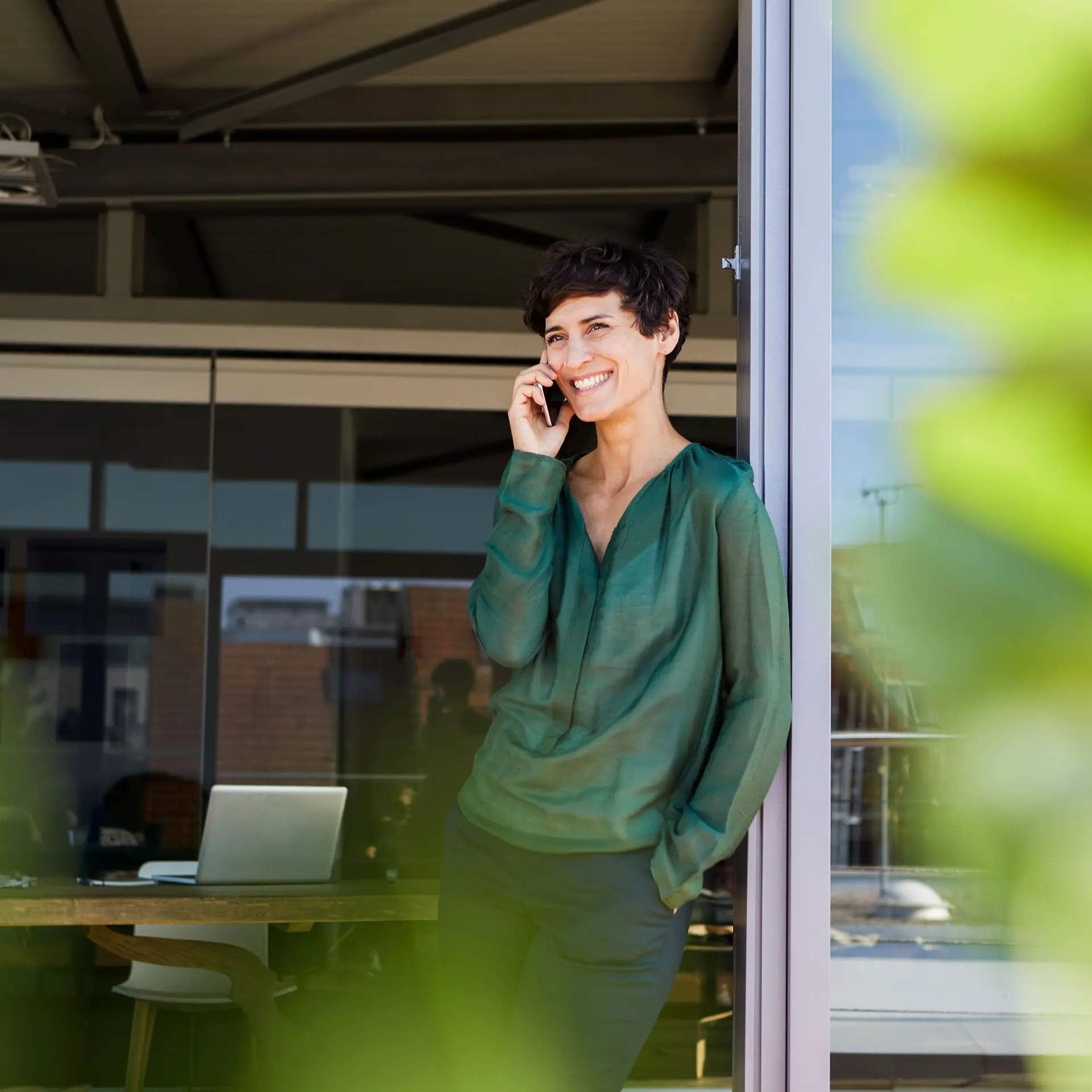 Lächelnde Frau lehnt an einer Schiebetür mit Handy am Ohr.