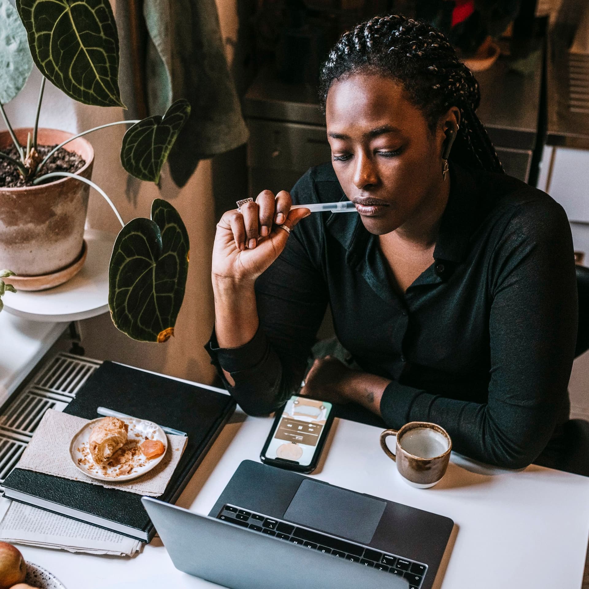 Junge Frau, die mit Laptop in einer Küche sitzt, während sie von zu Hause aus arbeitet.