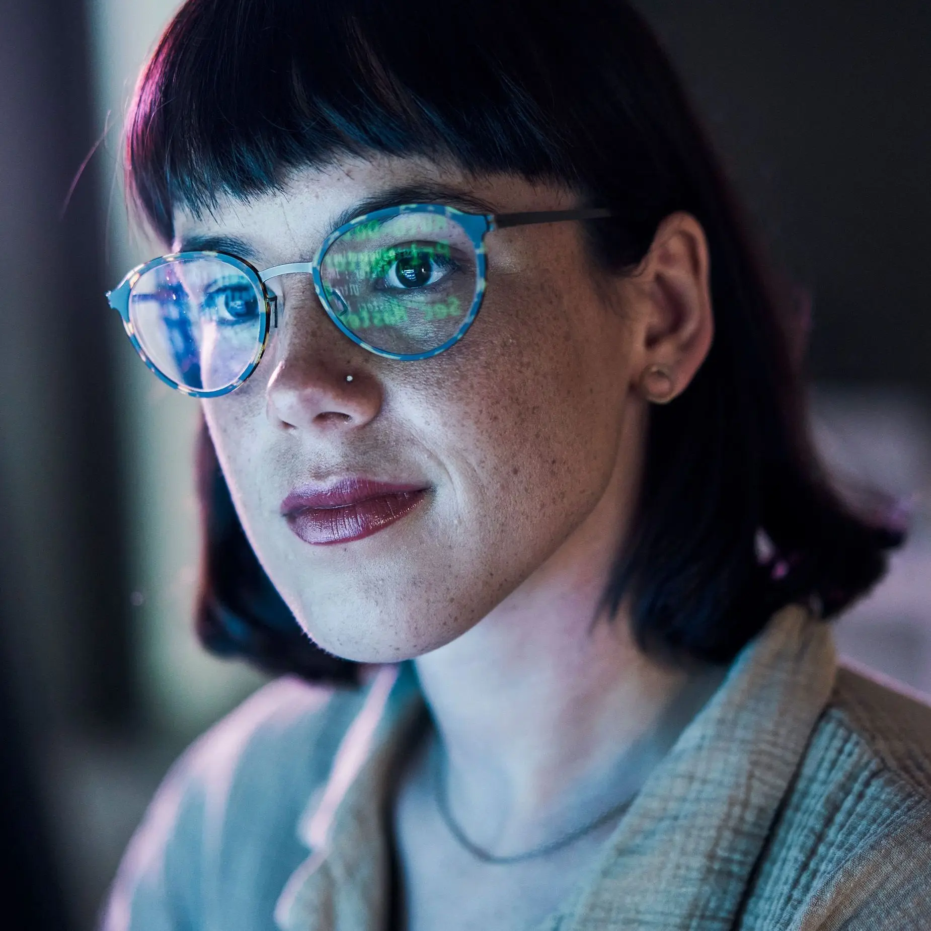 Ein Frau schaut lächelnd auf einen Monitor. Es spiegeln sich Zahlen auf ihrer Brille