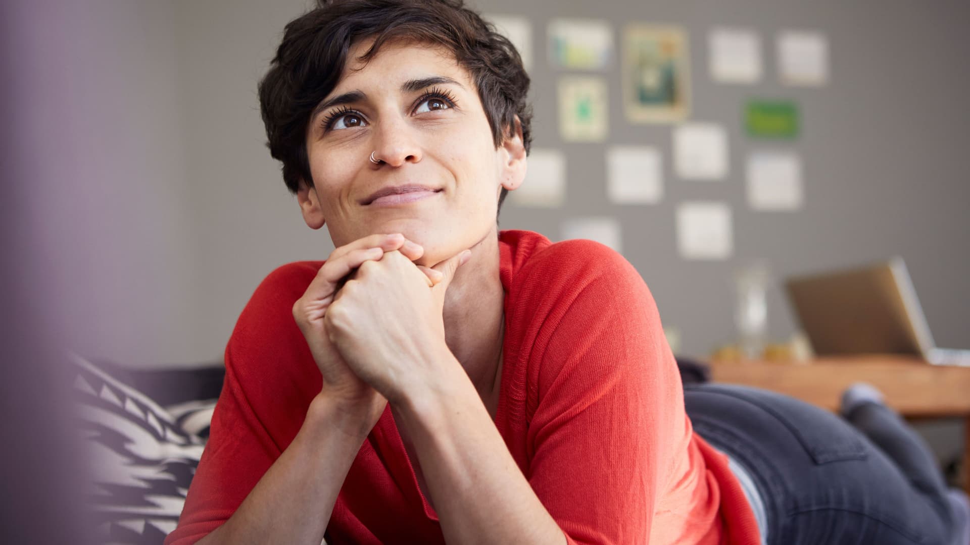 Portrait einer lächelnden jungen Frau, die bäuchlings auf dem Sofa liegt.