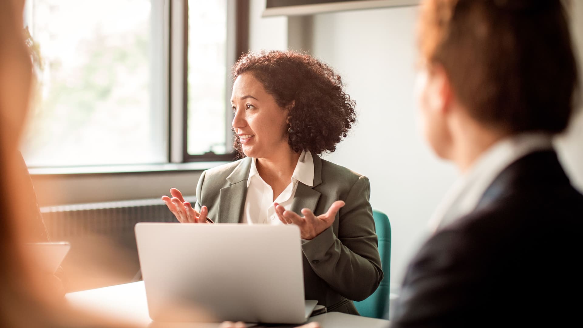 Mehrere Frauen sitzen zusammen bei einem Business Meeting in einem Konferenzraum. Man sieht eine Frau, die vor einem Laptop sitzt und mit den Händen gestikuliert.