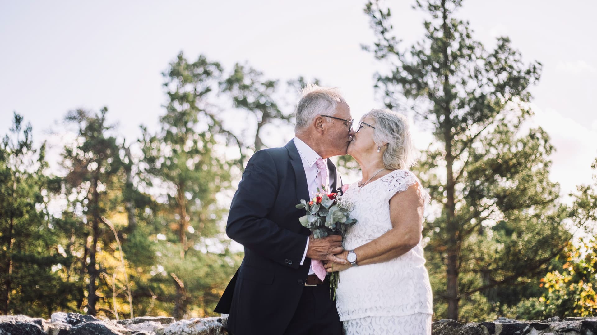 Liebevolles, frisch verheiratetes Seniorenpaar, das sich am Hochzeitstag vor dem Wald küsst