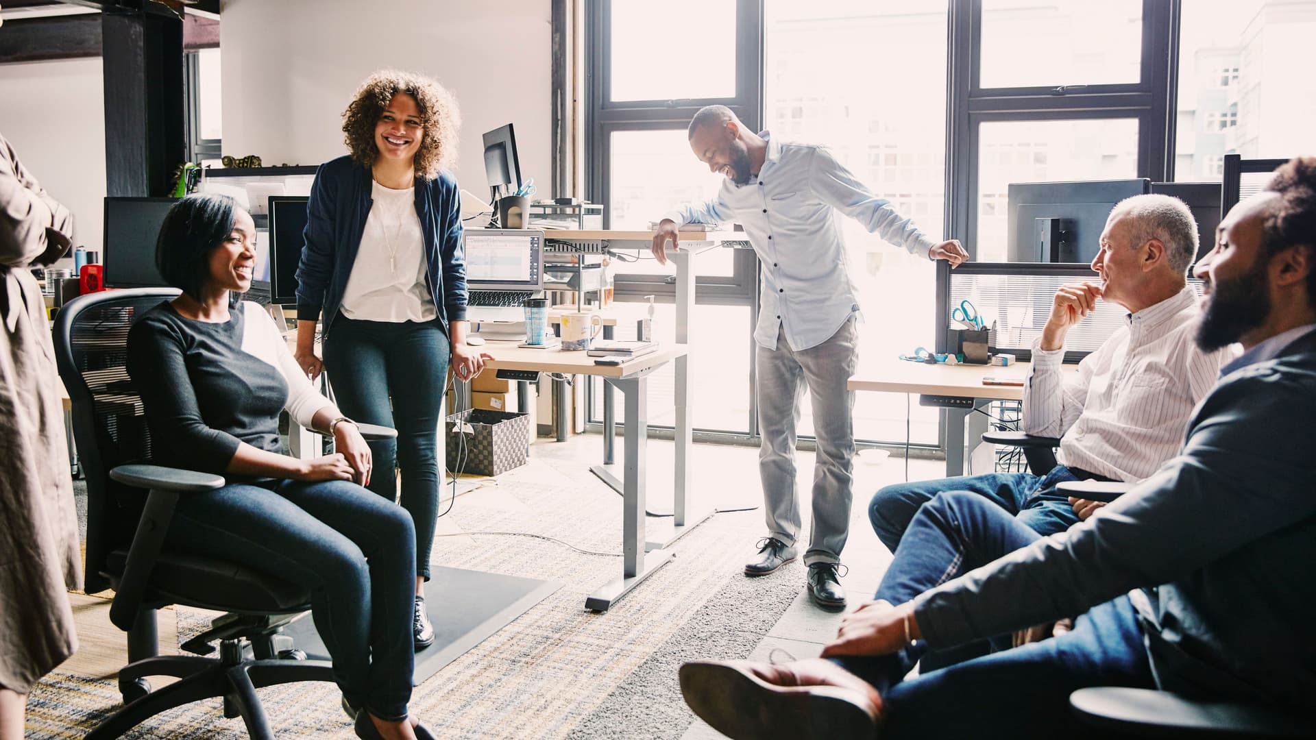 Mitarbeiter sitzen und stehen in einem Kreis bei einer Teambesprechung in einem modernen Büro.