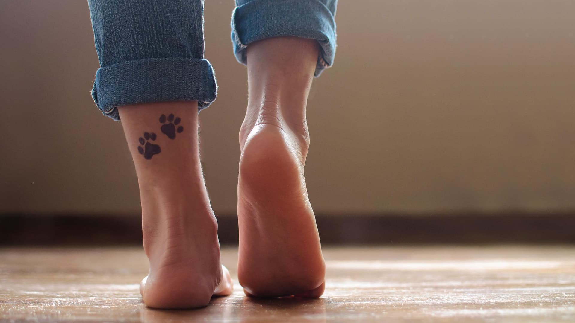 Nackte Fuess laufen auf einem Fliesenboden an der linken unteren Wade hat die Person 2 Pfoten taetowiert.